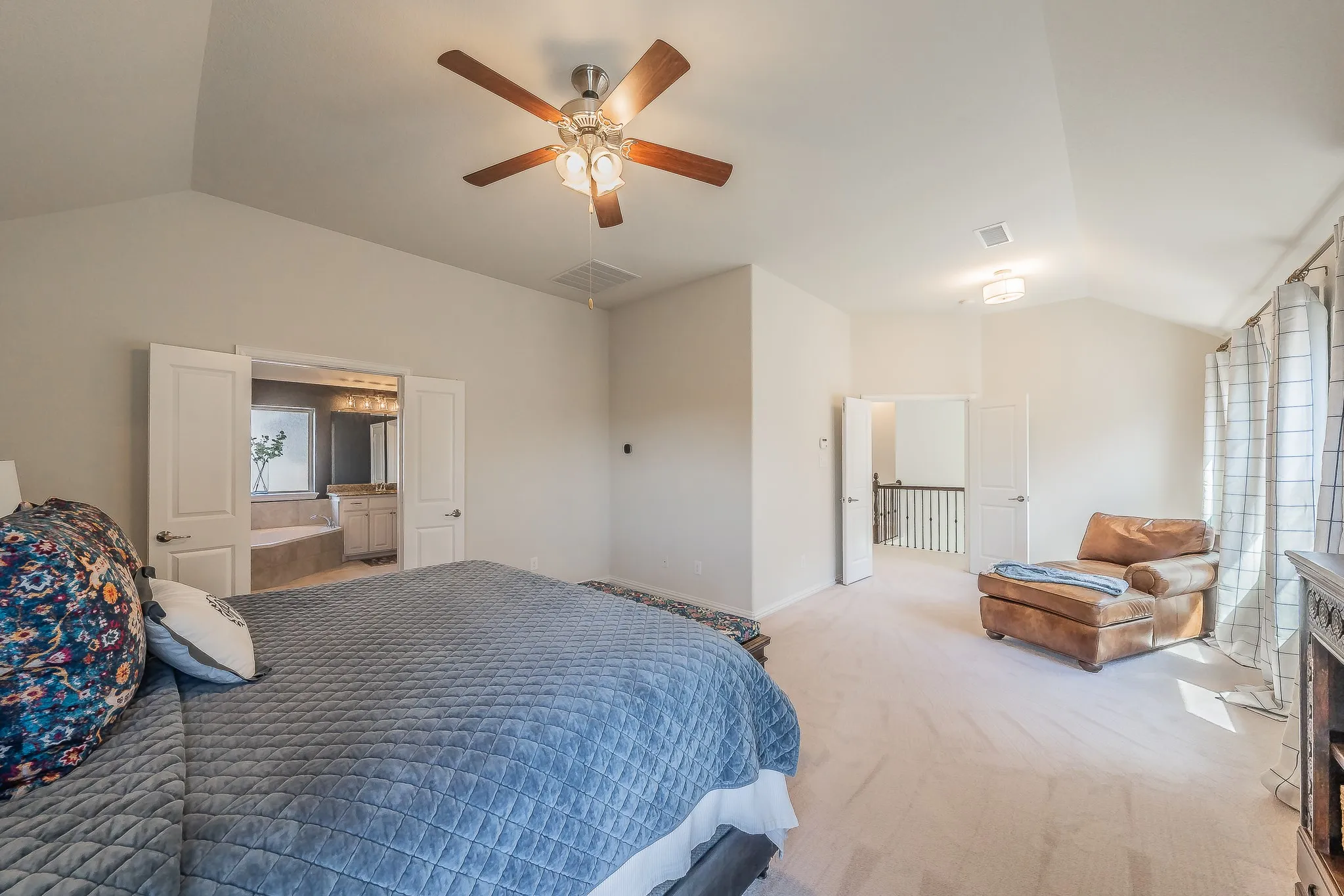 Vaulted ceiling with a ceiling fan, carpeted flooring, and a bath area with a built-in tub and vanity cabinet