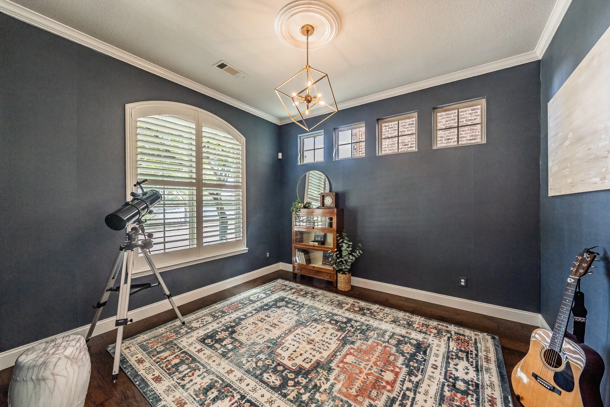 Hardwood-finish flooring with crown molding, arched window with plantation shutters, multiple transom windows, and a geometric chandelier