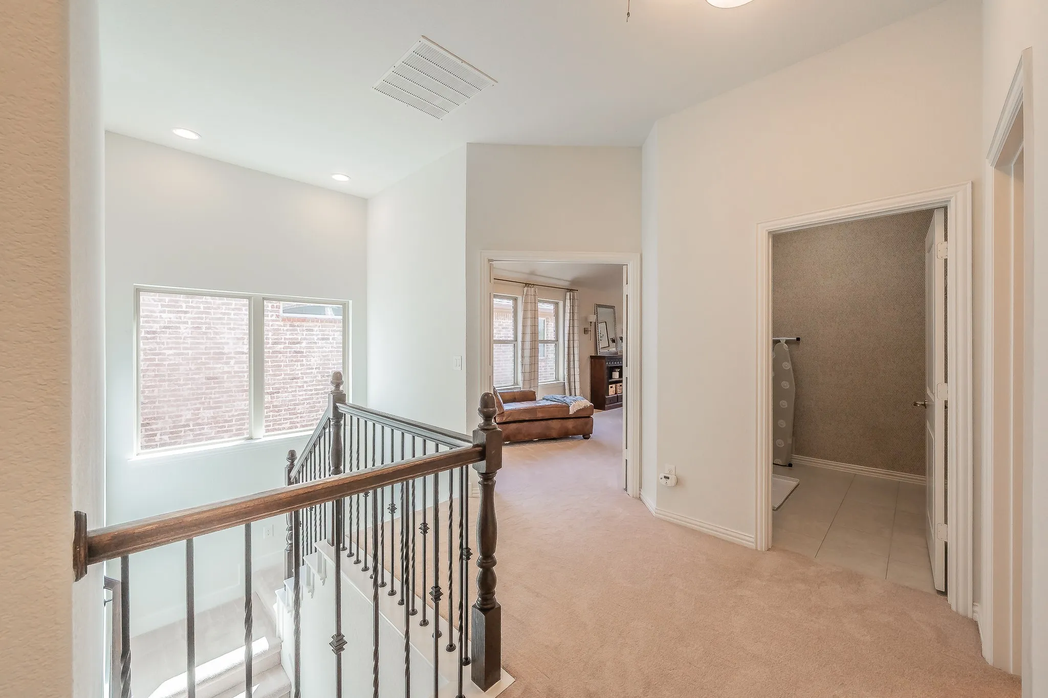 Upper-level hallway with carpet flooring, recessed lighting, and a staircase featuring a wooden handrail and wrought iron balusters
