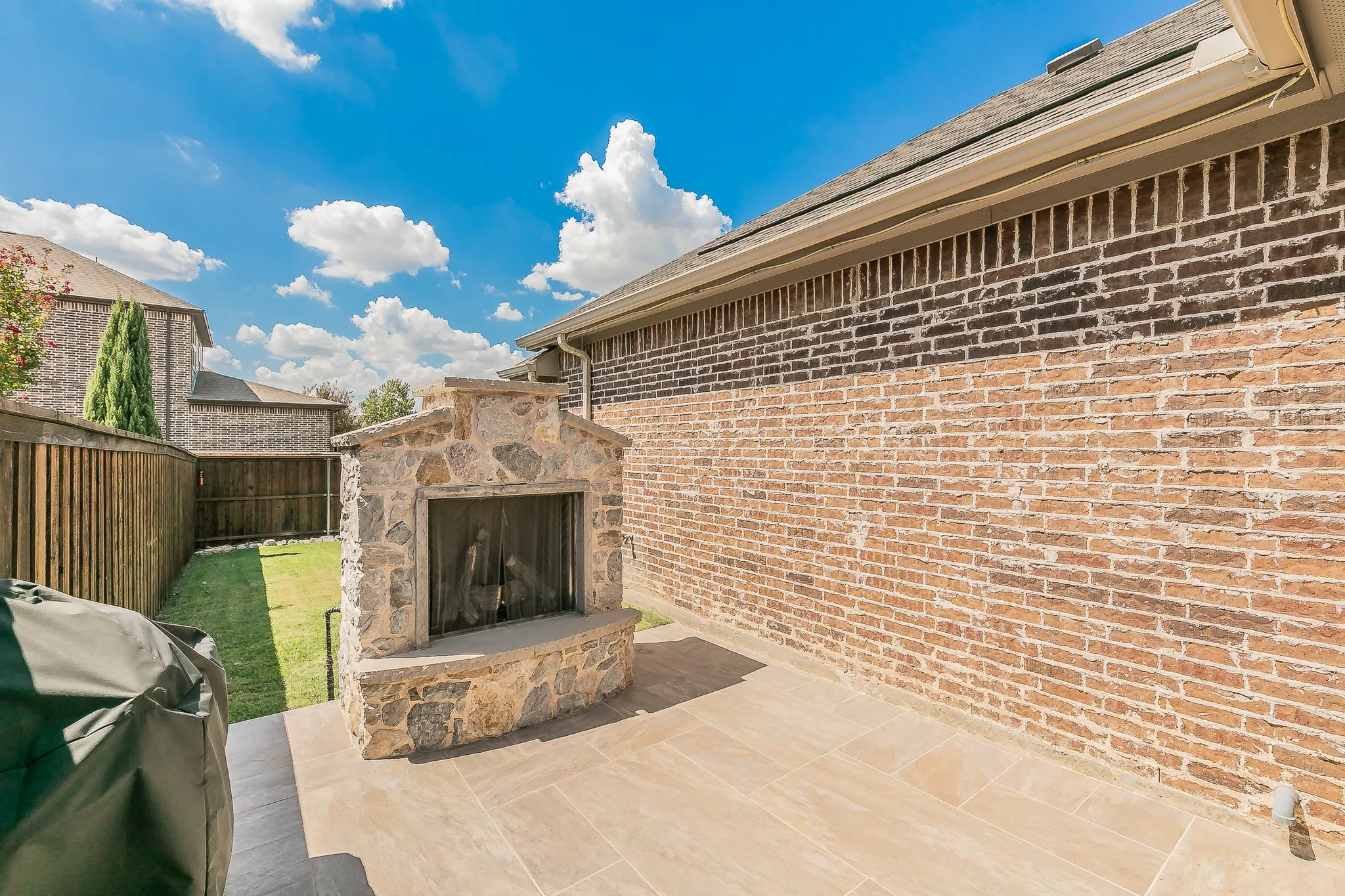 Outdoor patio with a stone-clad fireplace, brick exterior, and a manicured lawn