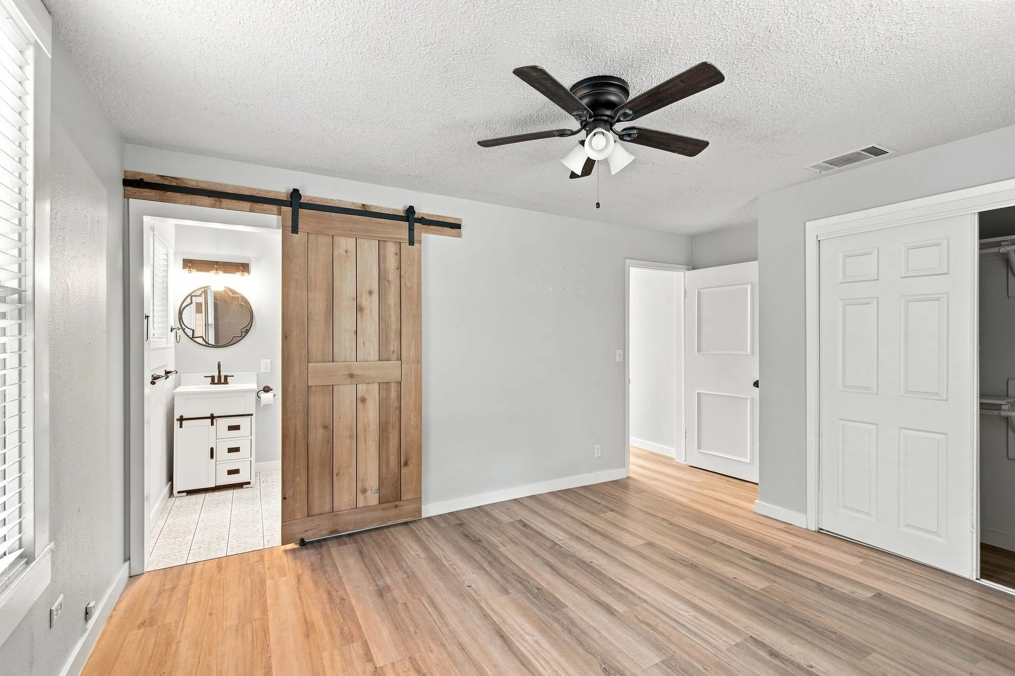 Wood-finish flooring, ceiling fan with integrated lighting, natural wood barn door, white paneled interior doors, and a closet with bifold doors