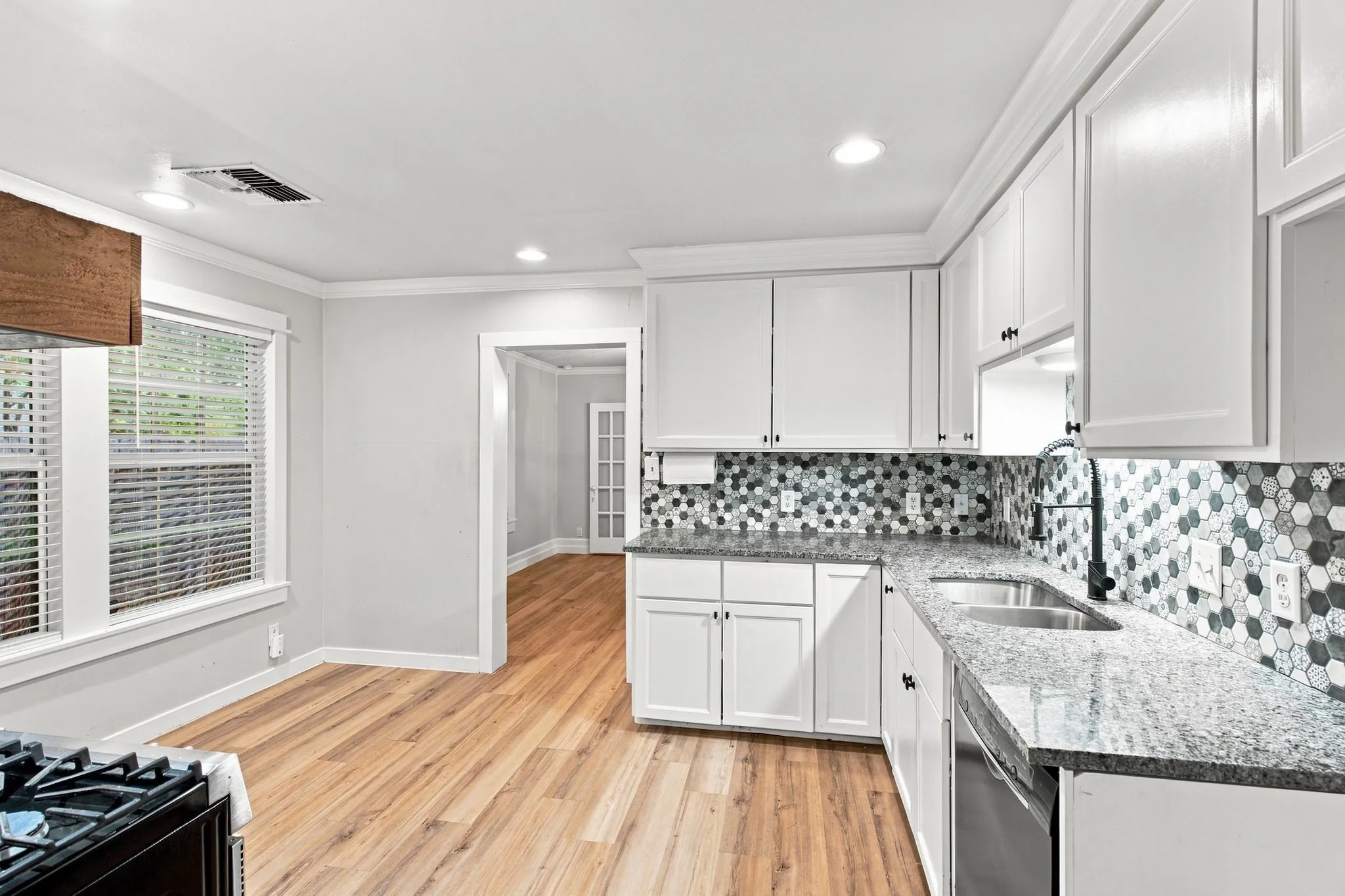 White cabinetry, stone countertops, hexagonal tile backsplash, stainless steel sink, and wood-finish flooring