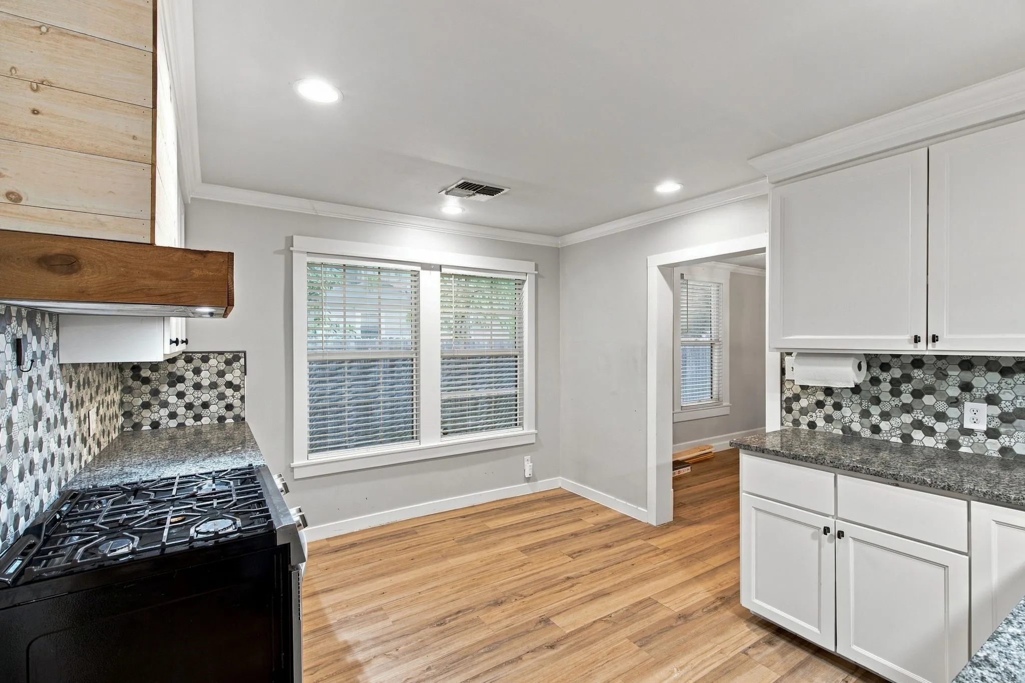 Wood-finish flooring, recessed lighting, white shaker-style cabinetry, dark speckled countertops, and a mosaic tile backsplash