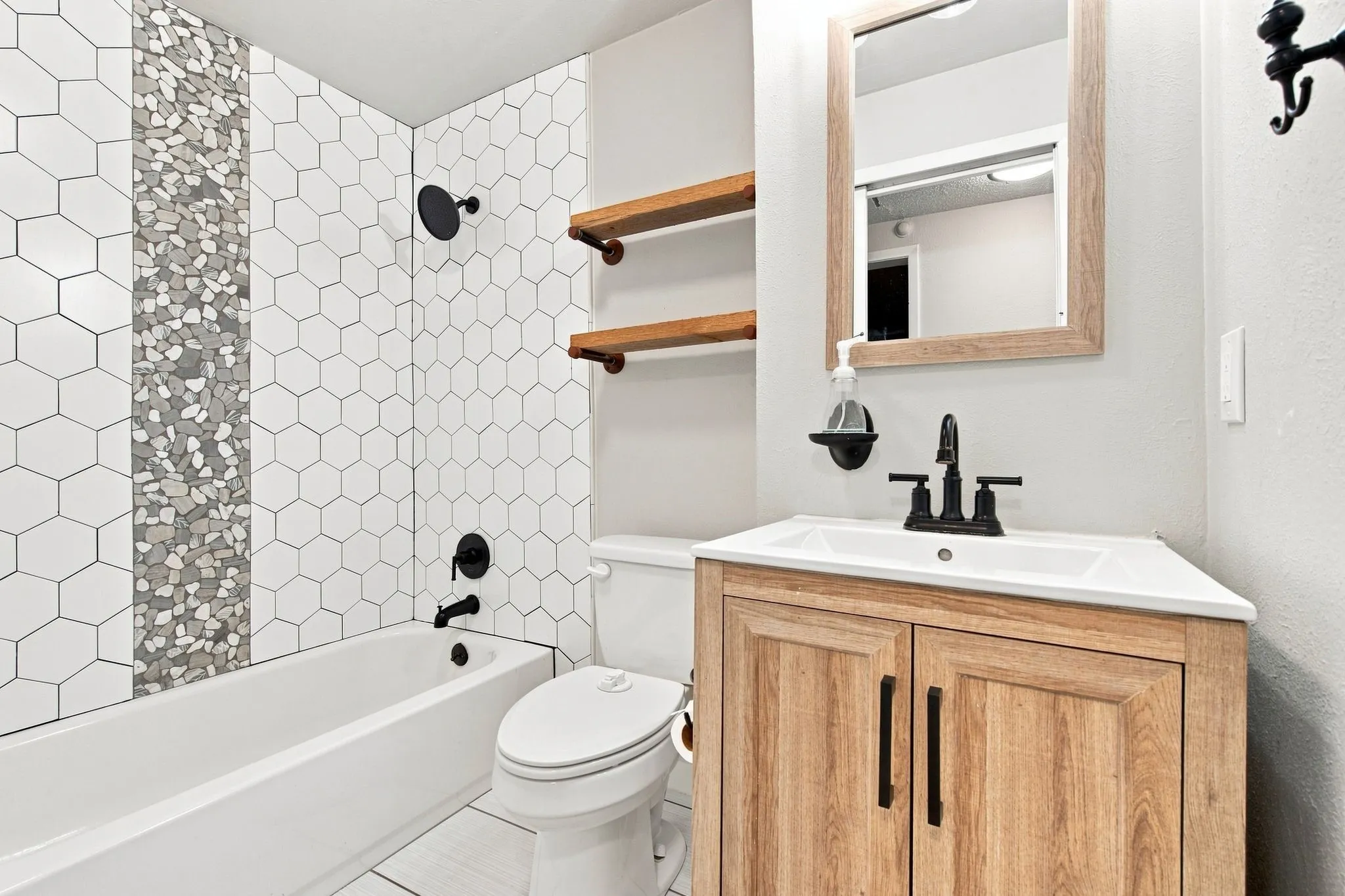 Bathroom featuring a white bathtub, hexagon tile shower surround with a decorative tile inlay, a light wood-finish vanity with a white countertop, and a framed mirror
