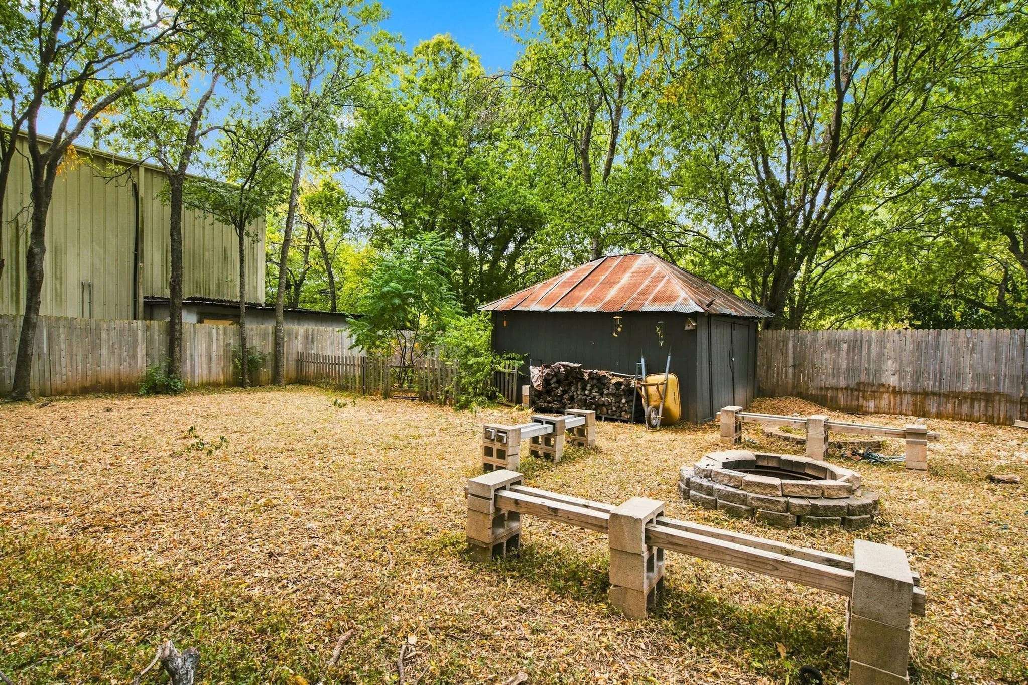 Expansive yard space featuring a stone fire pit, built-in seating, privacy fencing, and a storage shed with a metal roof