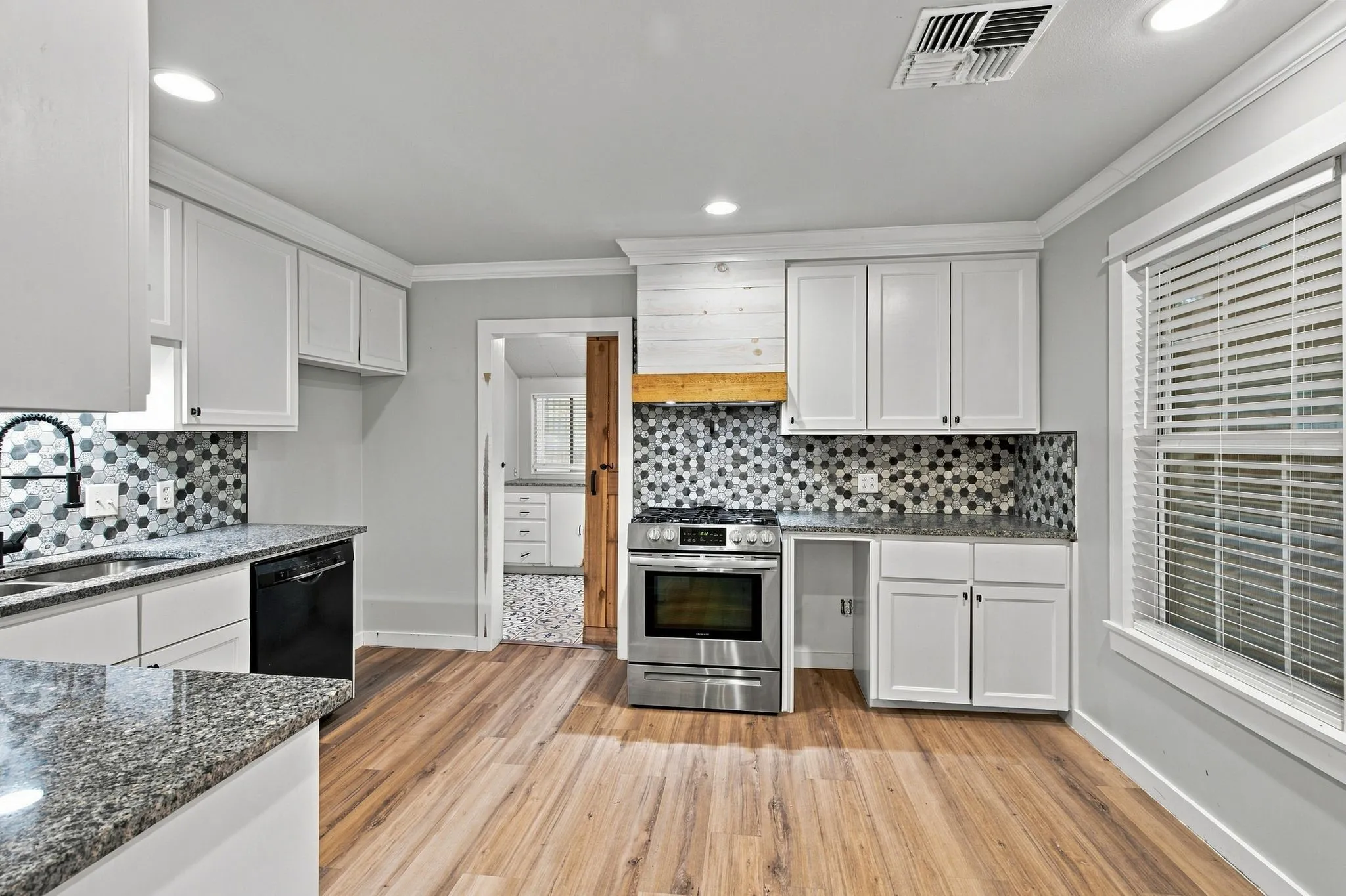 White cabinetry, tile backsplash, granite countertops, wood-finish flooring, and recessed lighting