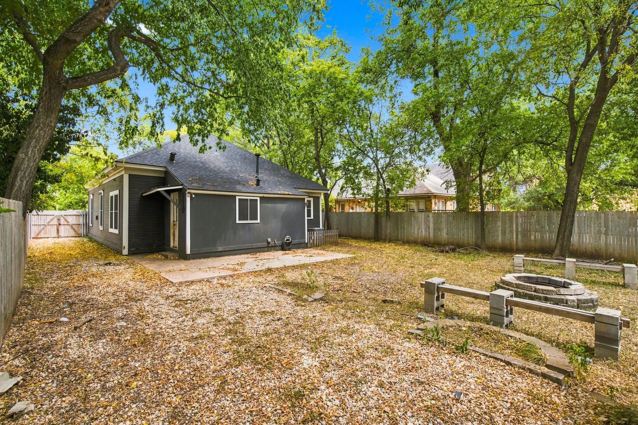 Expansive backyard with a dedicated fire pit area, surrounded by mature trees
