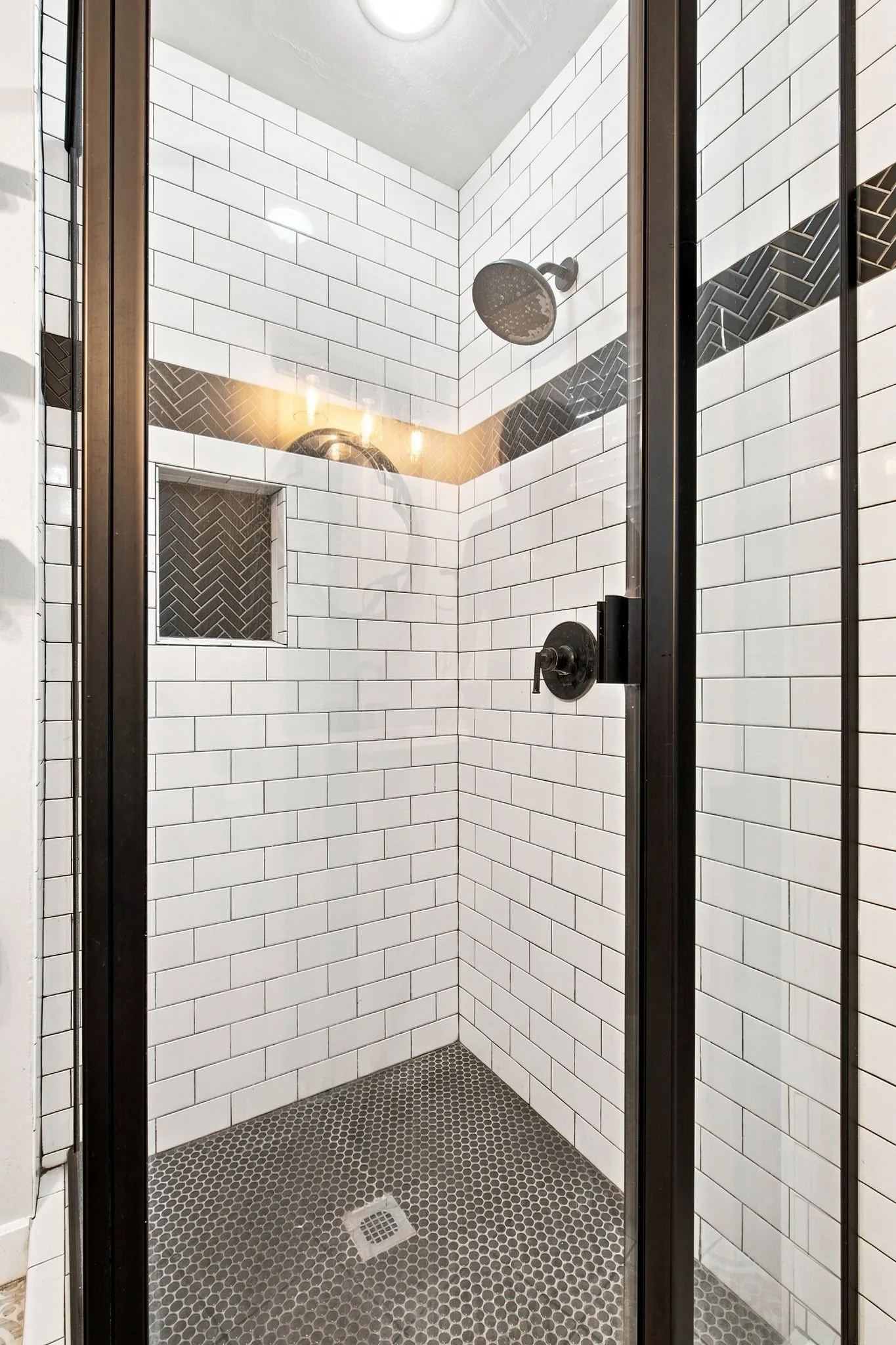 Shower enclosure with dark-framed glass, white subway tile walls, and a dark tile accent band