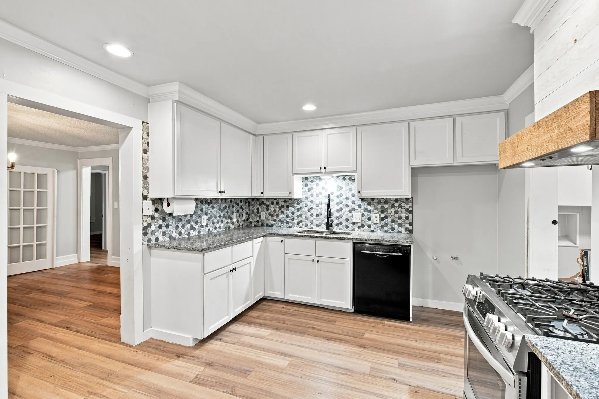 White cabinetry, mosaic tile backsplash, granite countertops, wood-finish flooring, and a stainless steel gas range