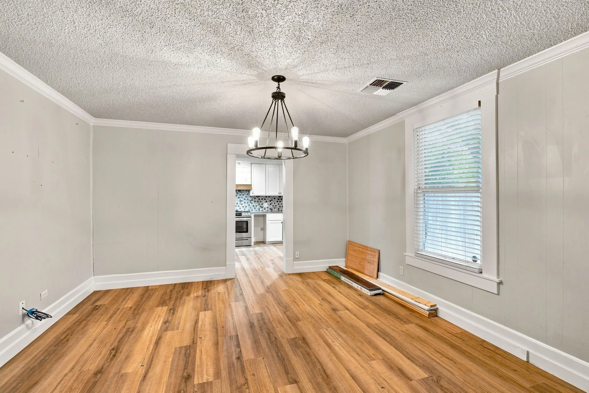 Wood-finish flooring, crown molding, and a modern chandelier