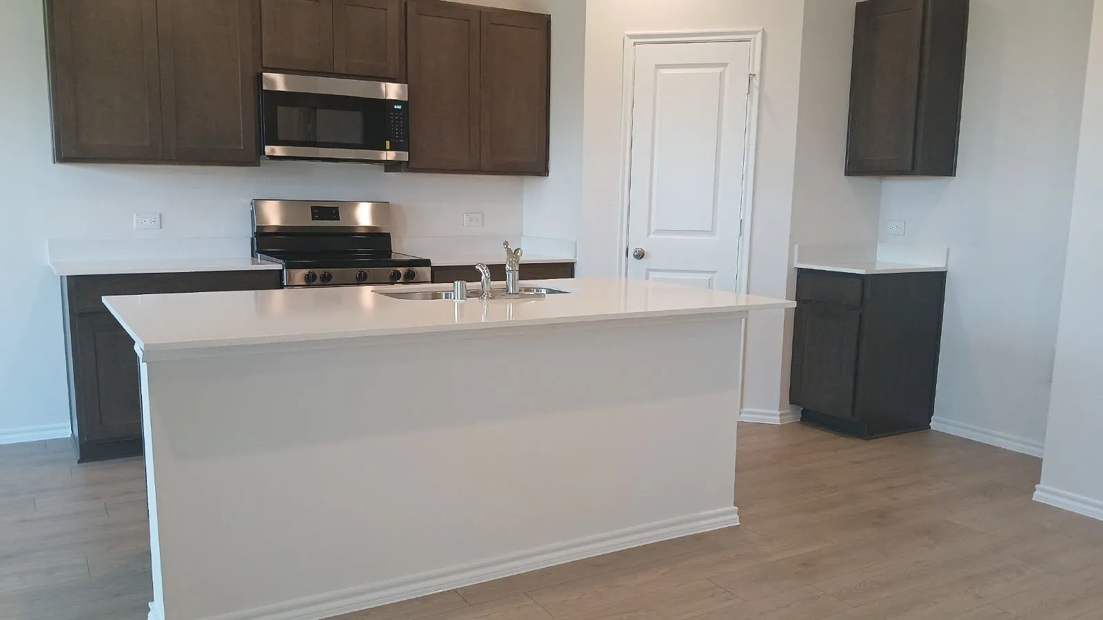 Kitchen featuring an expansive island with an undermount sink, stainless steel appliances, dark wood-finish cabinetry, and light countertops