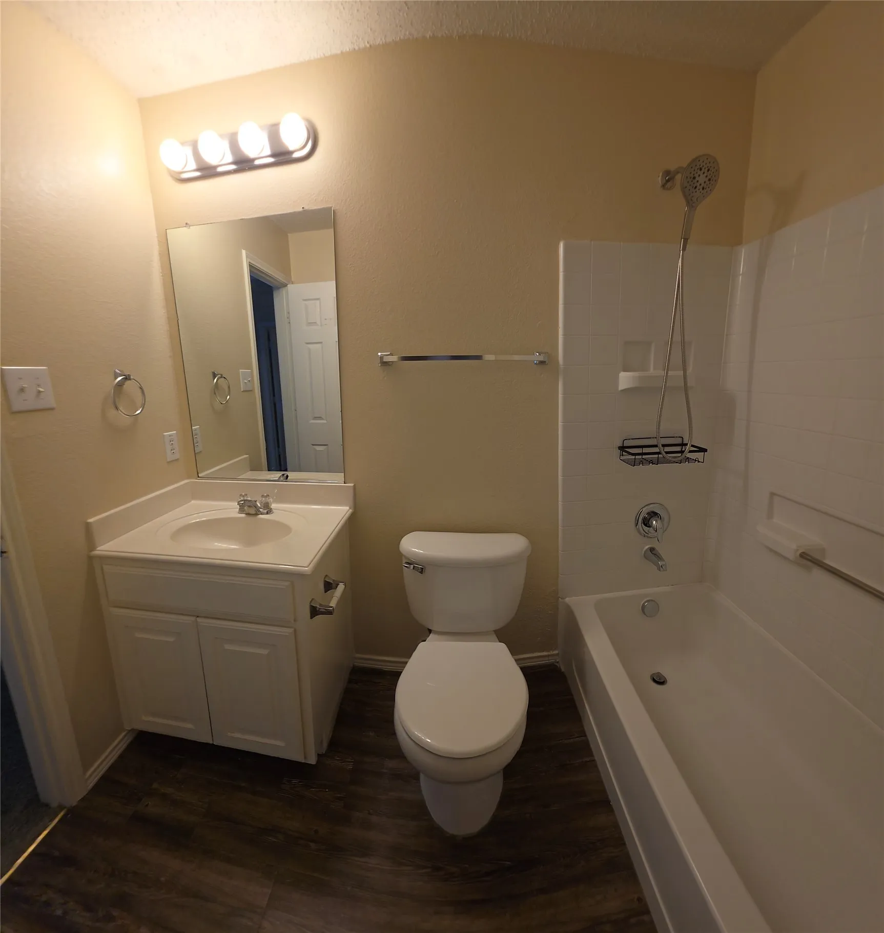 Full bathroom featuring a white vanity with integrated sink, wood-finish flooring, a toilet, and a bathtub with a tiled surround