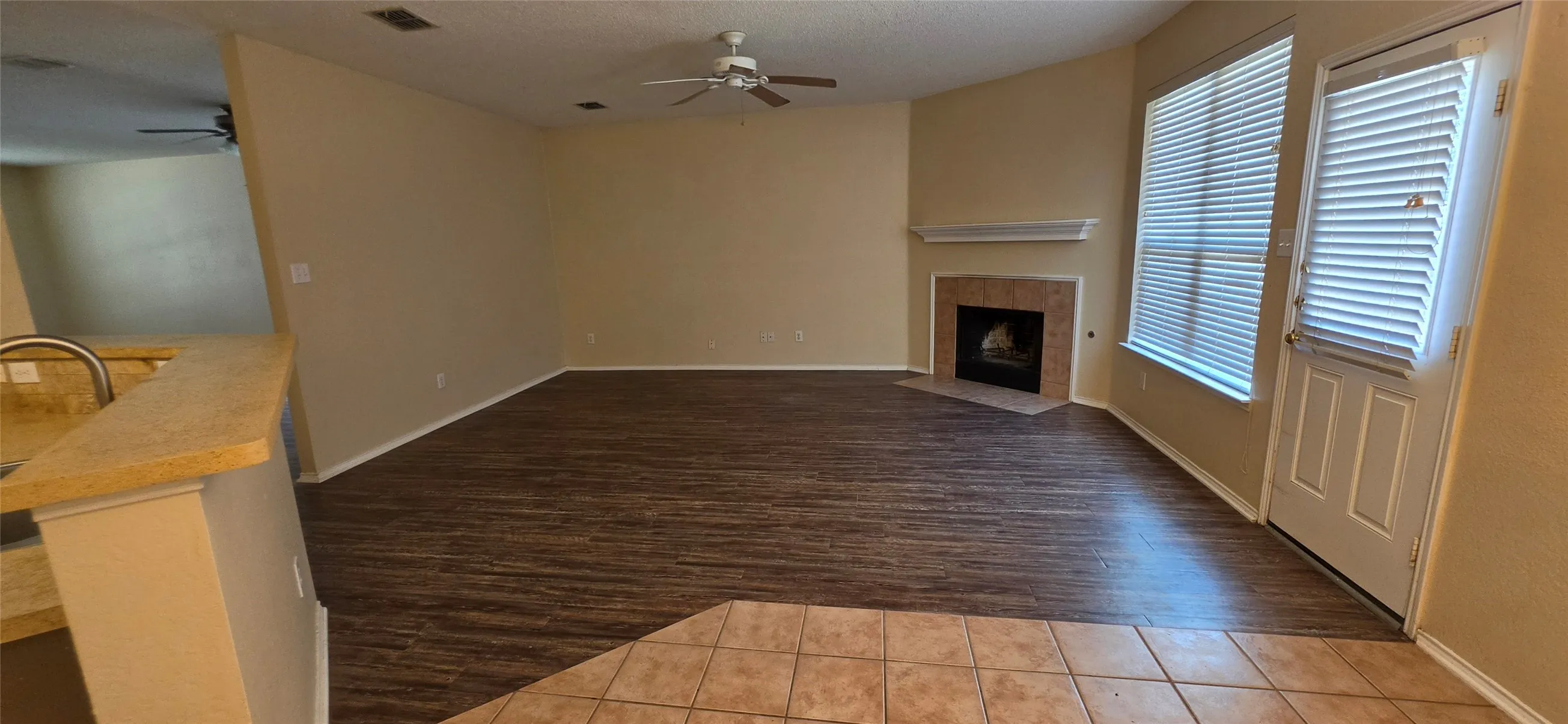 Spacious living area featuring wood-finish flooring, a corner fireplace with a tiled surround and mantel, and a ceiling fan