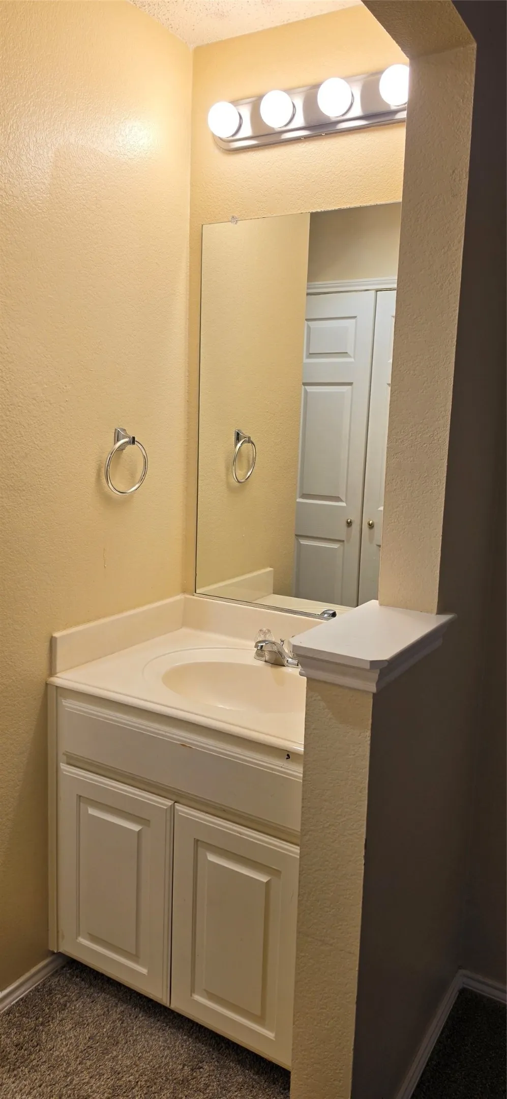 Vanity with an integrated sink, white cabinetry, wall-mounted mirror, and a four-bulb vanity light fixture