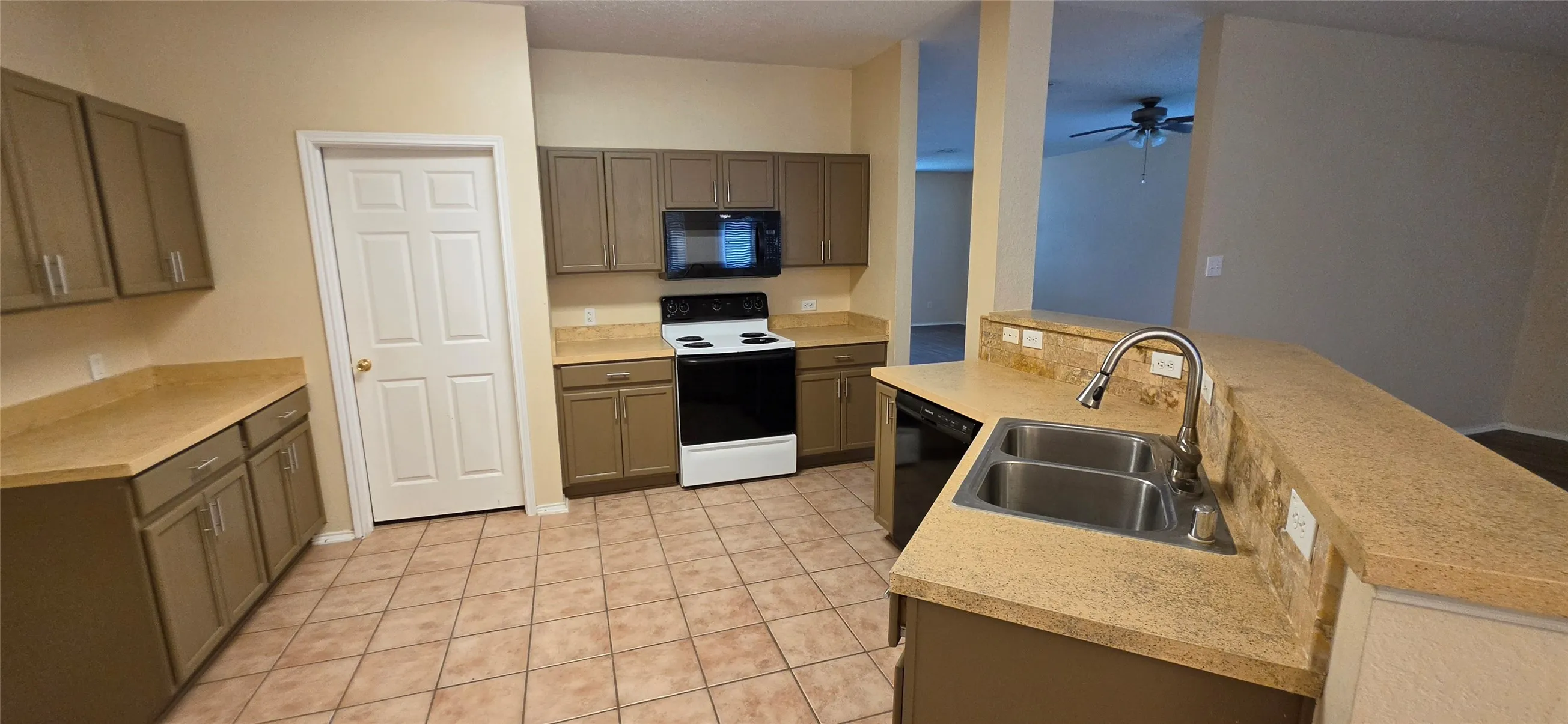 Kitchen featuring tile flooring, dual basin stainless steel sink with pull-down faucet, brown cabinetry, and light-toned countertops
