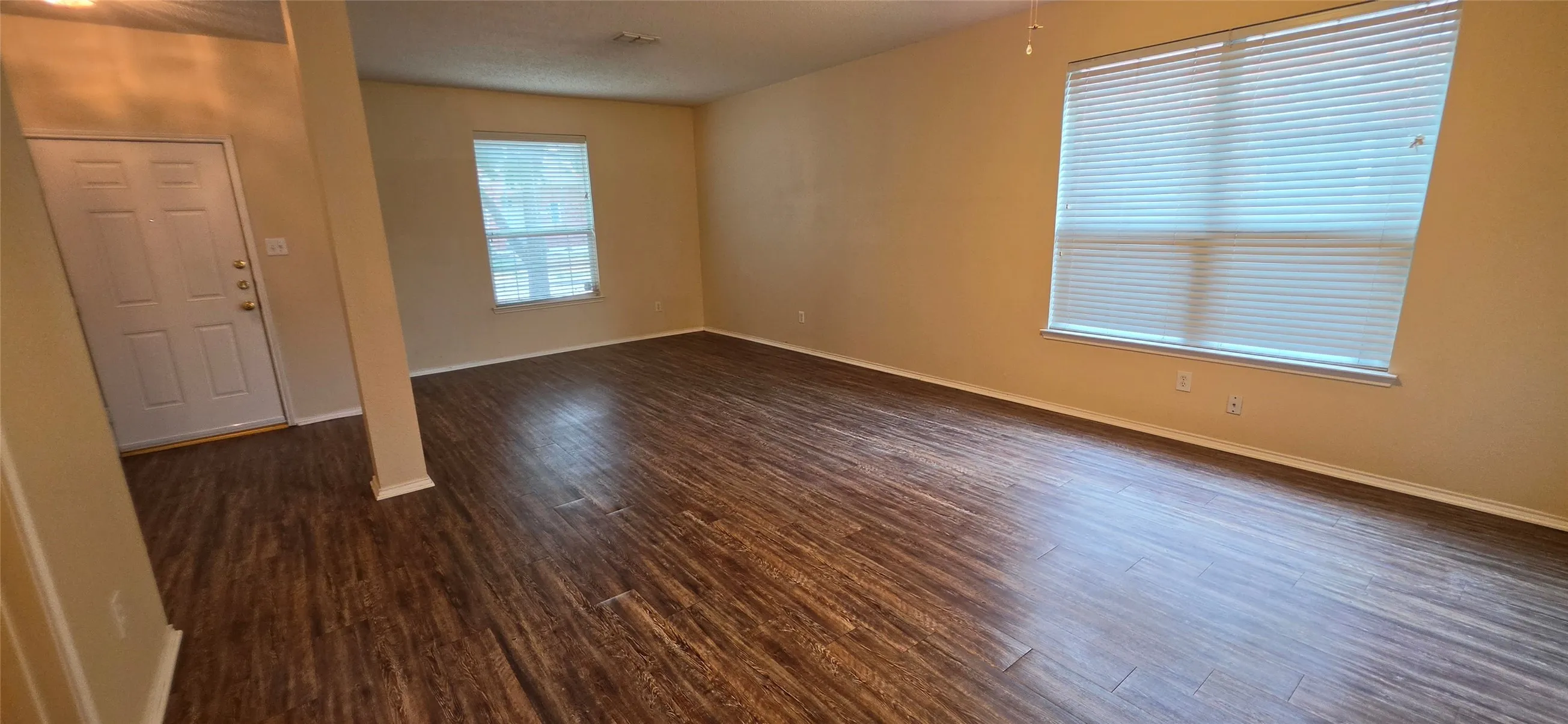 Spacious room featuring wood-finish flooring, multiple windows with blinds, and neutral wall tones