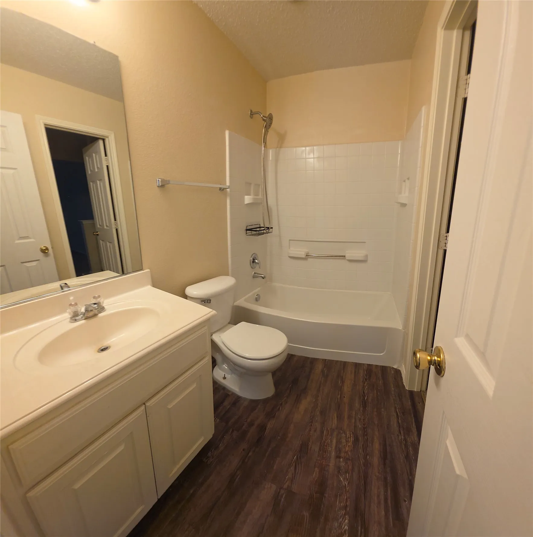 Bathroom featuring wood-finish flooring, a white vanity with an integrated sink, a large wall mirror, and a tub/shower combination with white tile surround
