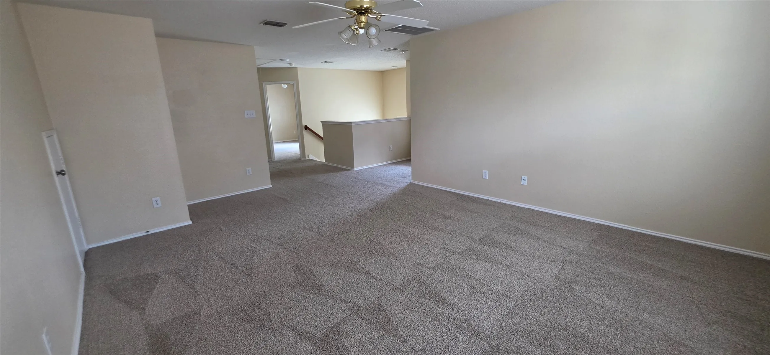 Expansive carpeted floor with a geometric pattern, neutral wall tones, and a ceiling fan with integrated lighting