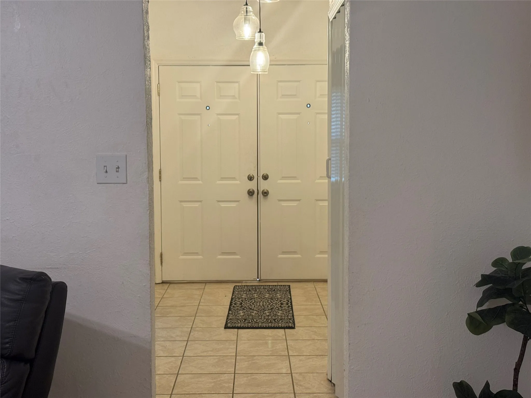 Double entry doors with paneled design, tile flooring, and pendant lighting fixtures