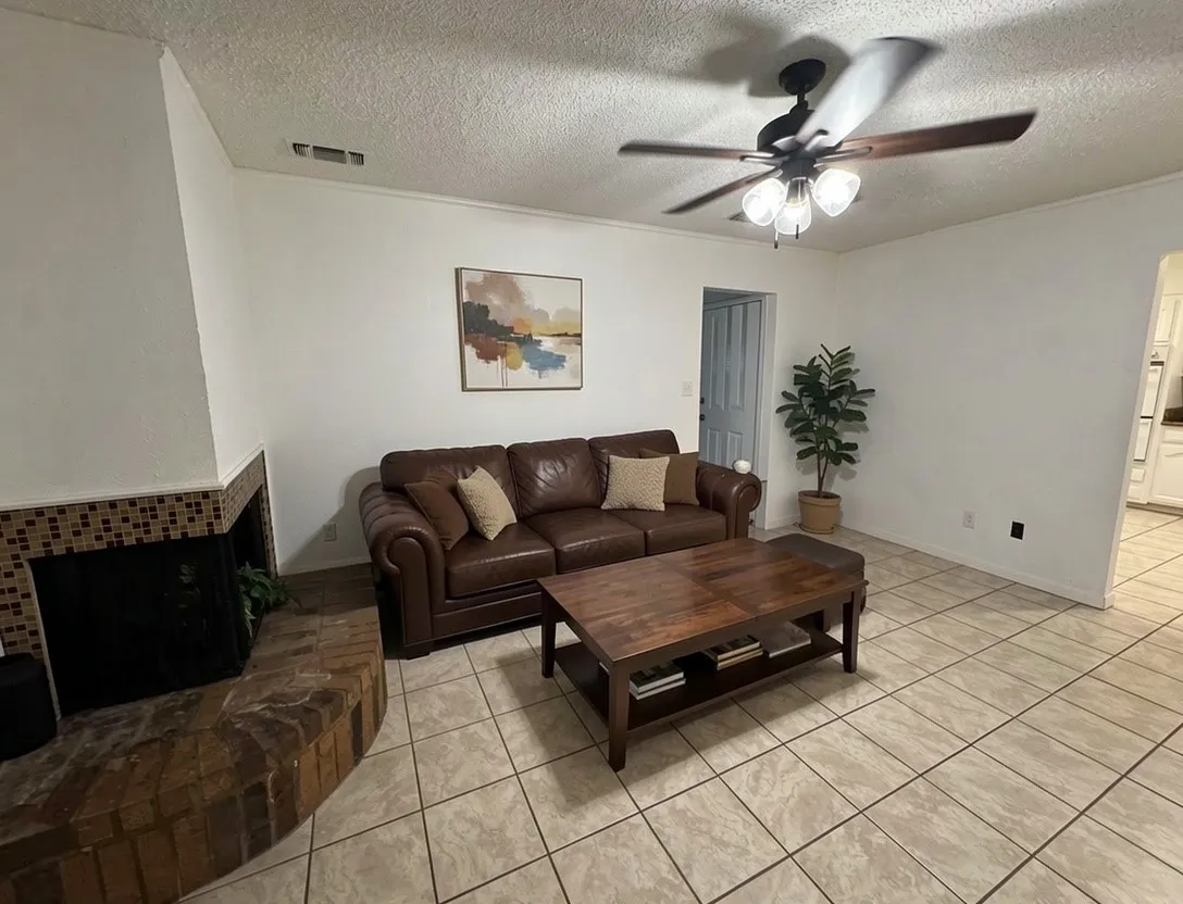 Second living area with ceramic tile flooring, brick fireplace, ceiling fan with light fixture, and neutral painted walls - virtually staged