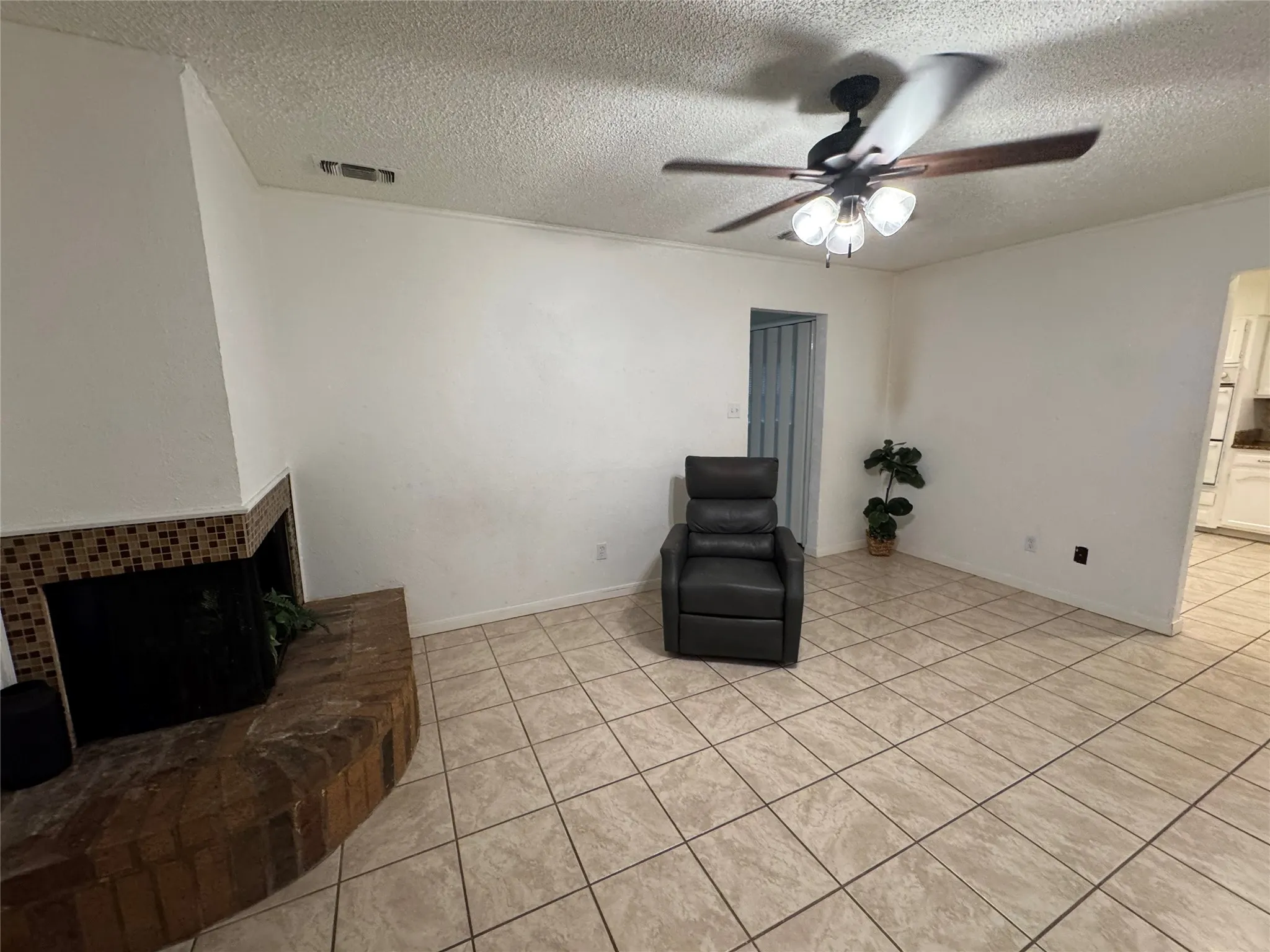 Tiled flooring, corner fireplace with brick hearth, ceiling fan with integrated lighting, and neutral wall tones