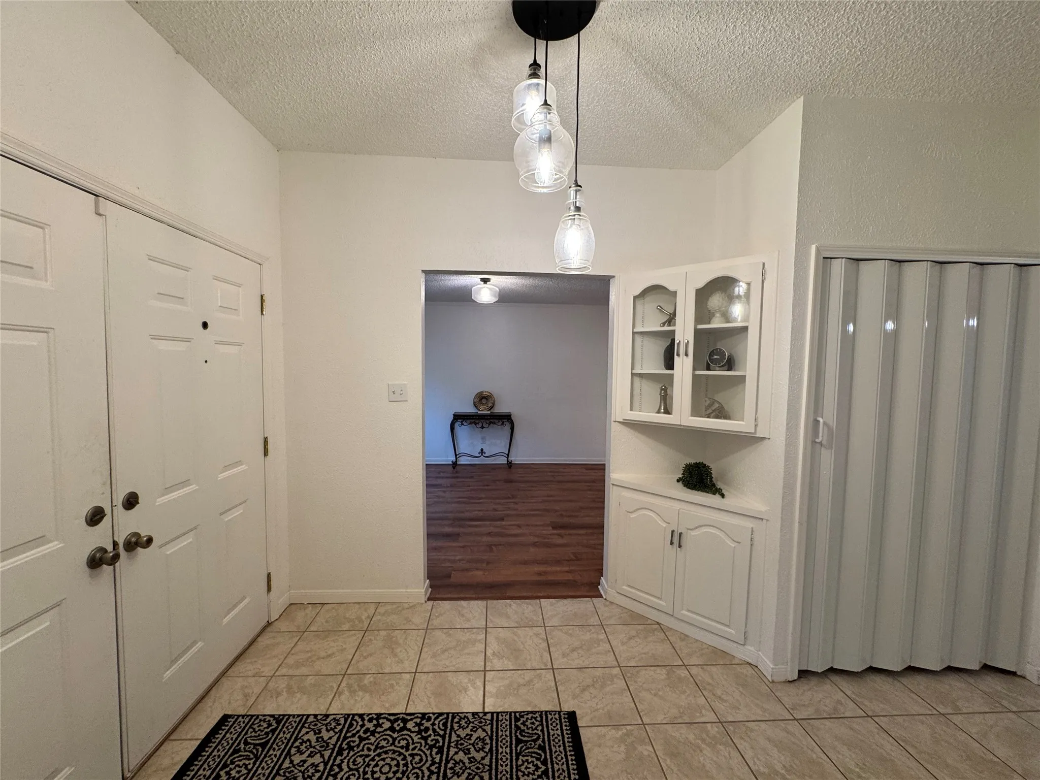 Tile flooring entry with a built-in corner cabinet featuring glass-front doors