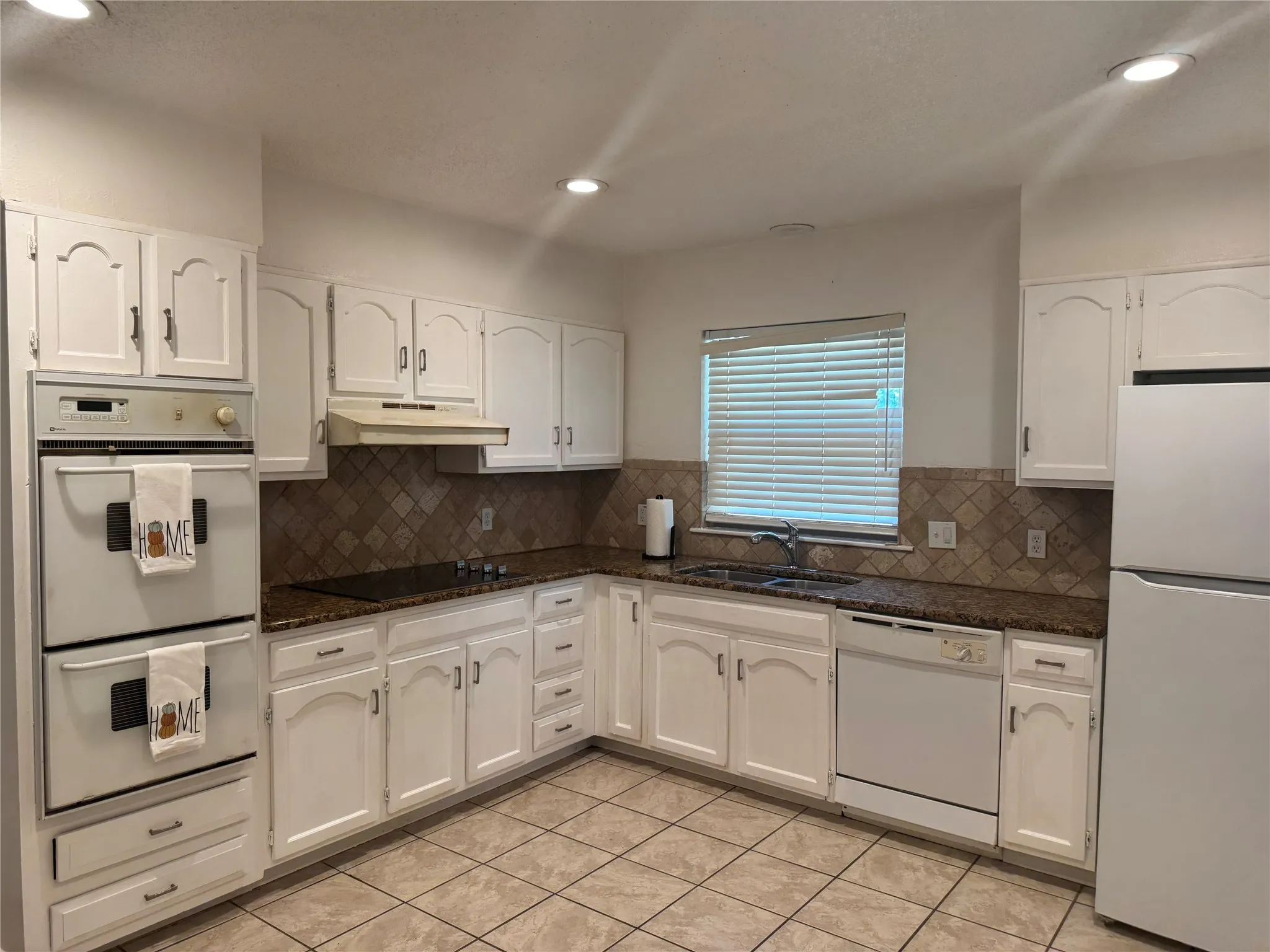 Kitchen featuring white cabinetry, granite-style countertops, mosaic tile backsplash, integrated double ovens, and a built-in dishwasher