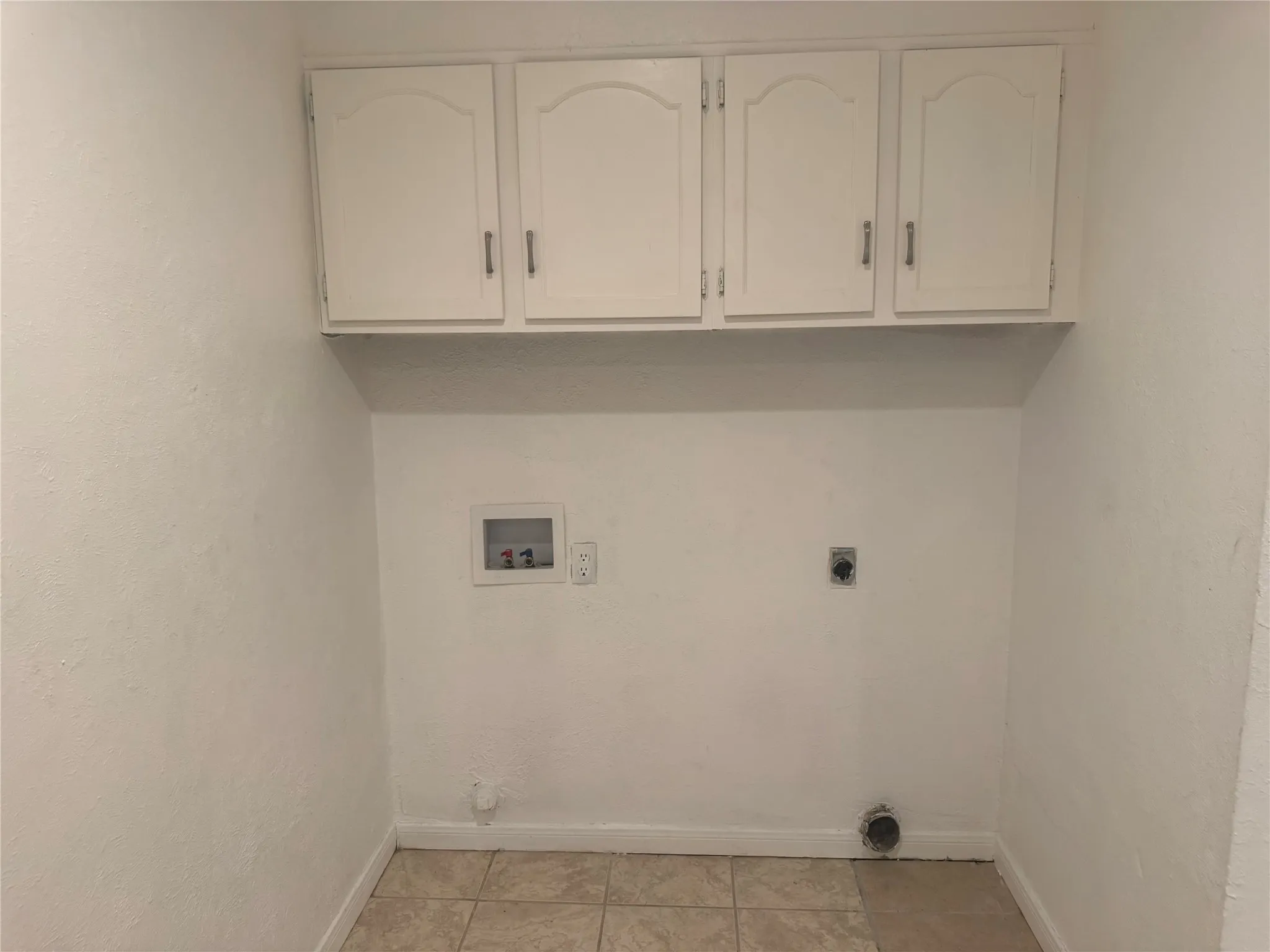 White upper cabinetry, tiled flooring, and utility hookups