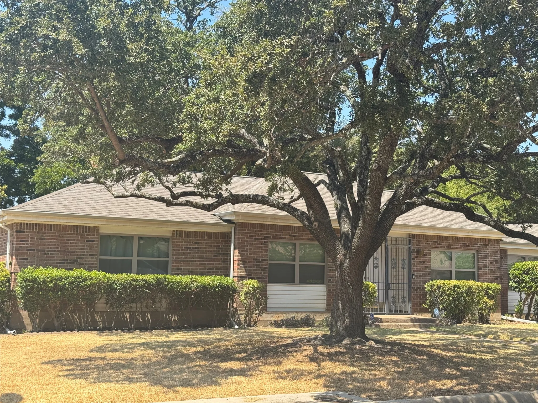 Brick exterior with a shingle roof and mature trees