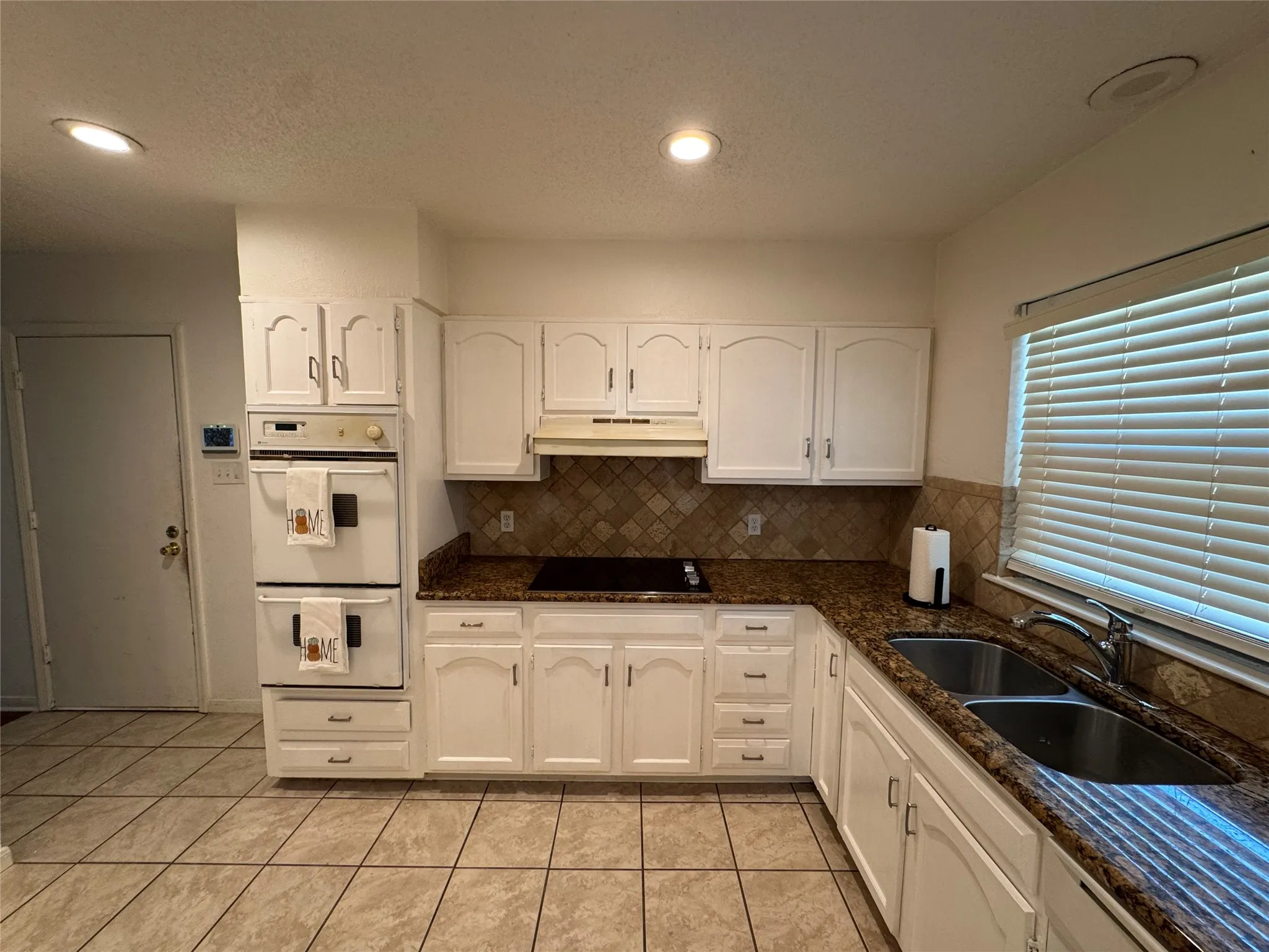 White cabinetry, built-in double oven, dual basin sink, patterned tile backsplash, and recessed lighting