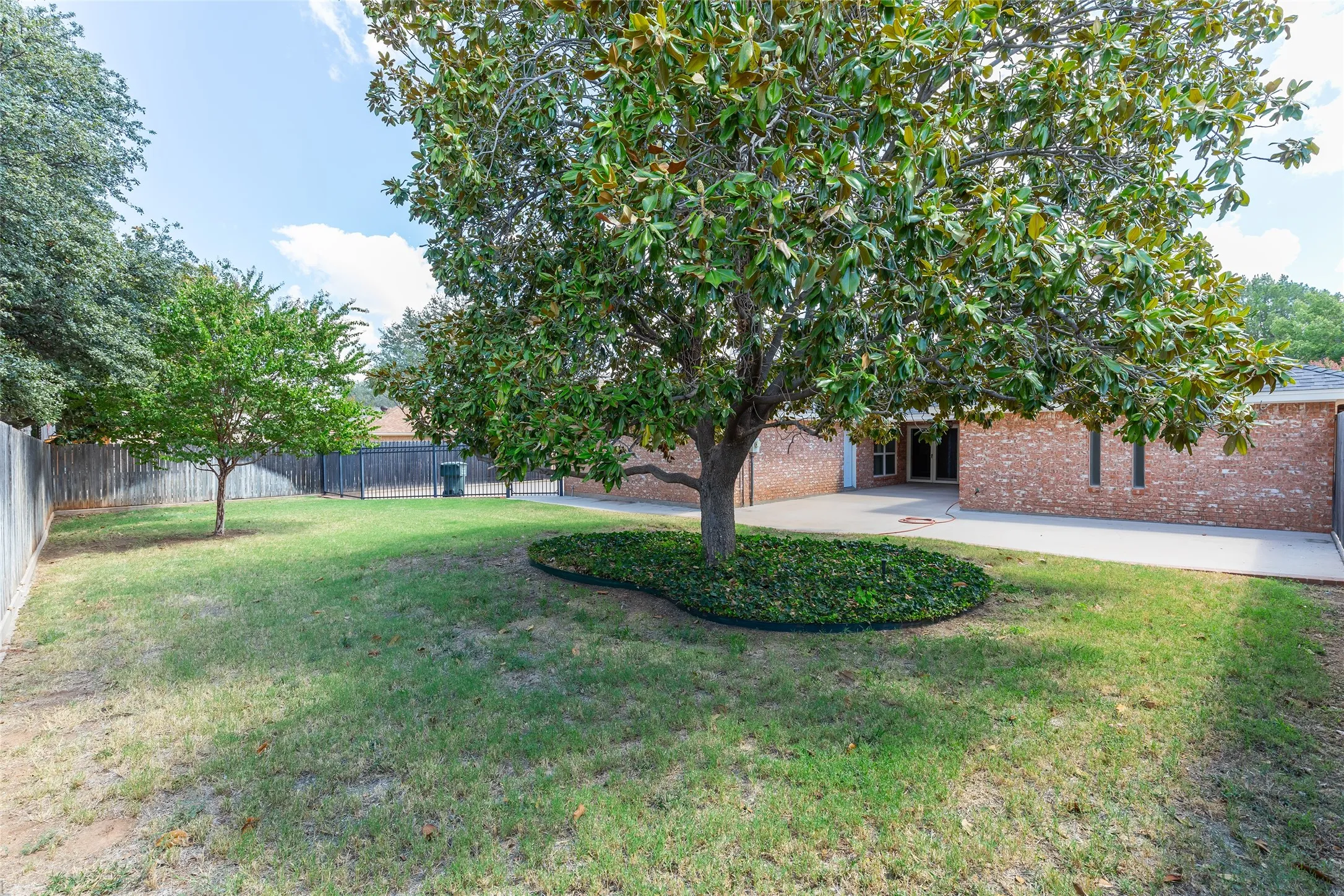 Expansive grounds featuring a mature shade tree with lush canopy, manicured lawn, and brick architectural elements