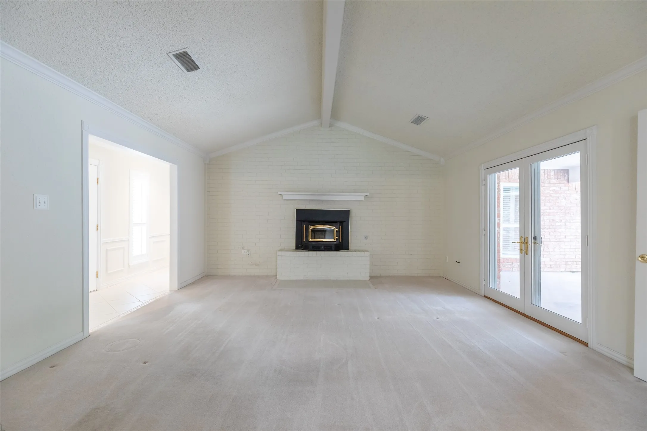 Vaulted ceiling with exposed beam, brick fireplace with mantel, double glass panel doors, and a cased opening