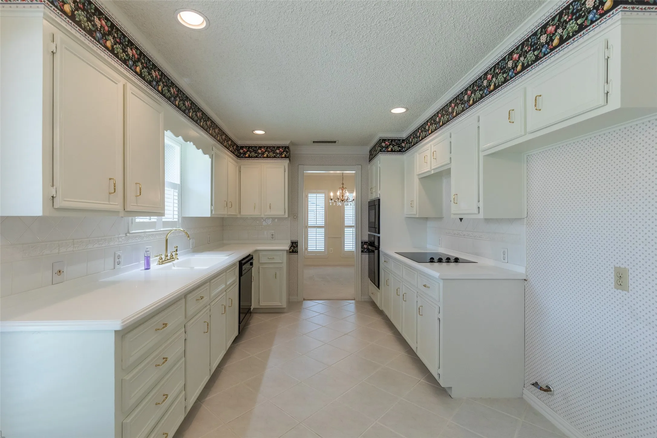 White cabinetry with gold-tone hardware, white countertops, built-in wall oven and microwave, and a ceramic cooktop