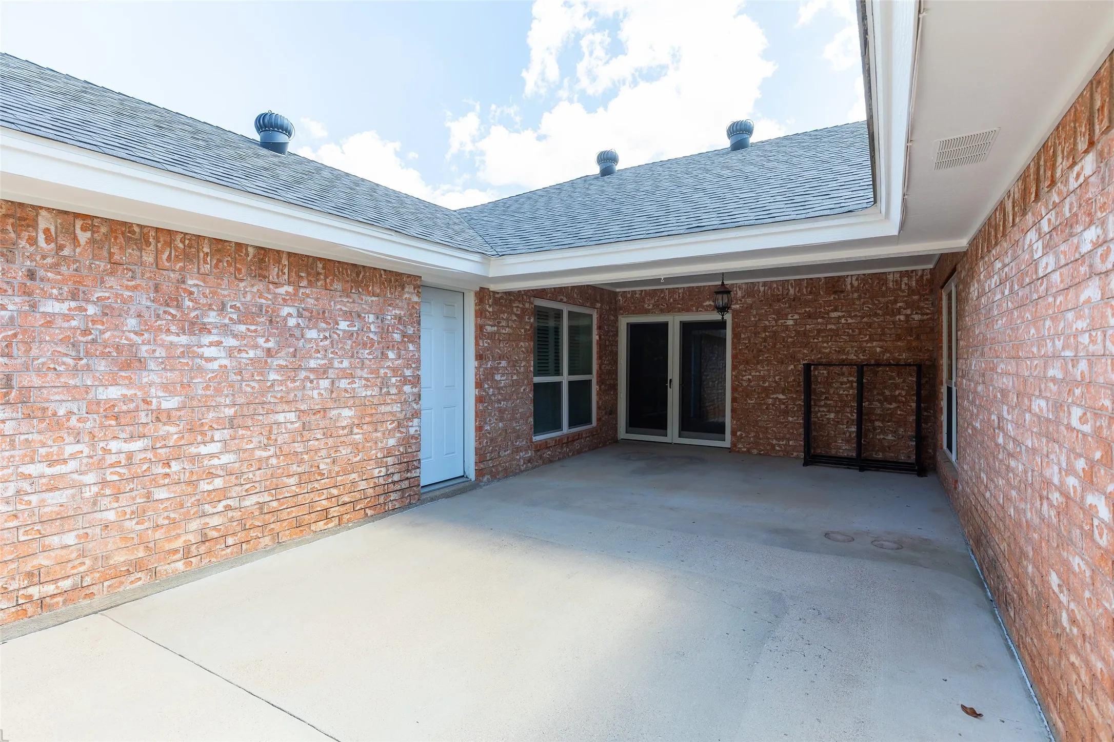 Covered patio featuring brick exterior, concrete flooring, and an outdoor light fixture