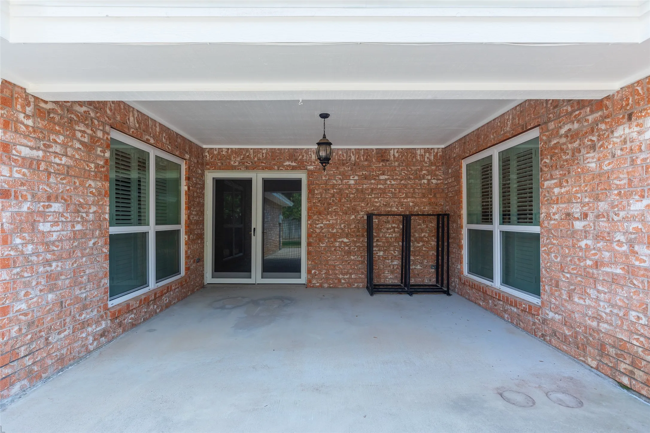 Spacious covered patio with exposed brick walls, concrete flooring, and multiple glass-paneled doors providing natural light