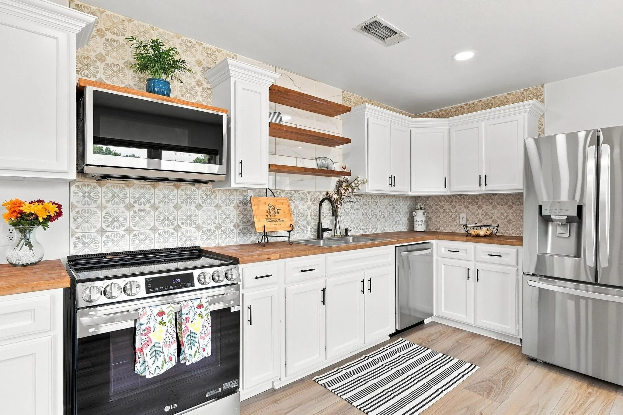 White cabinetry, wood-finish countertops, stainless steel appliances, patterned tile backsplash, and wood-finish flooring