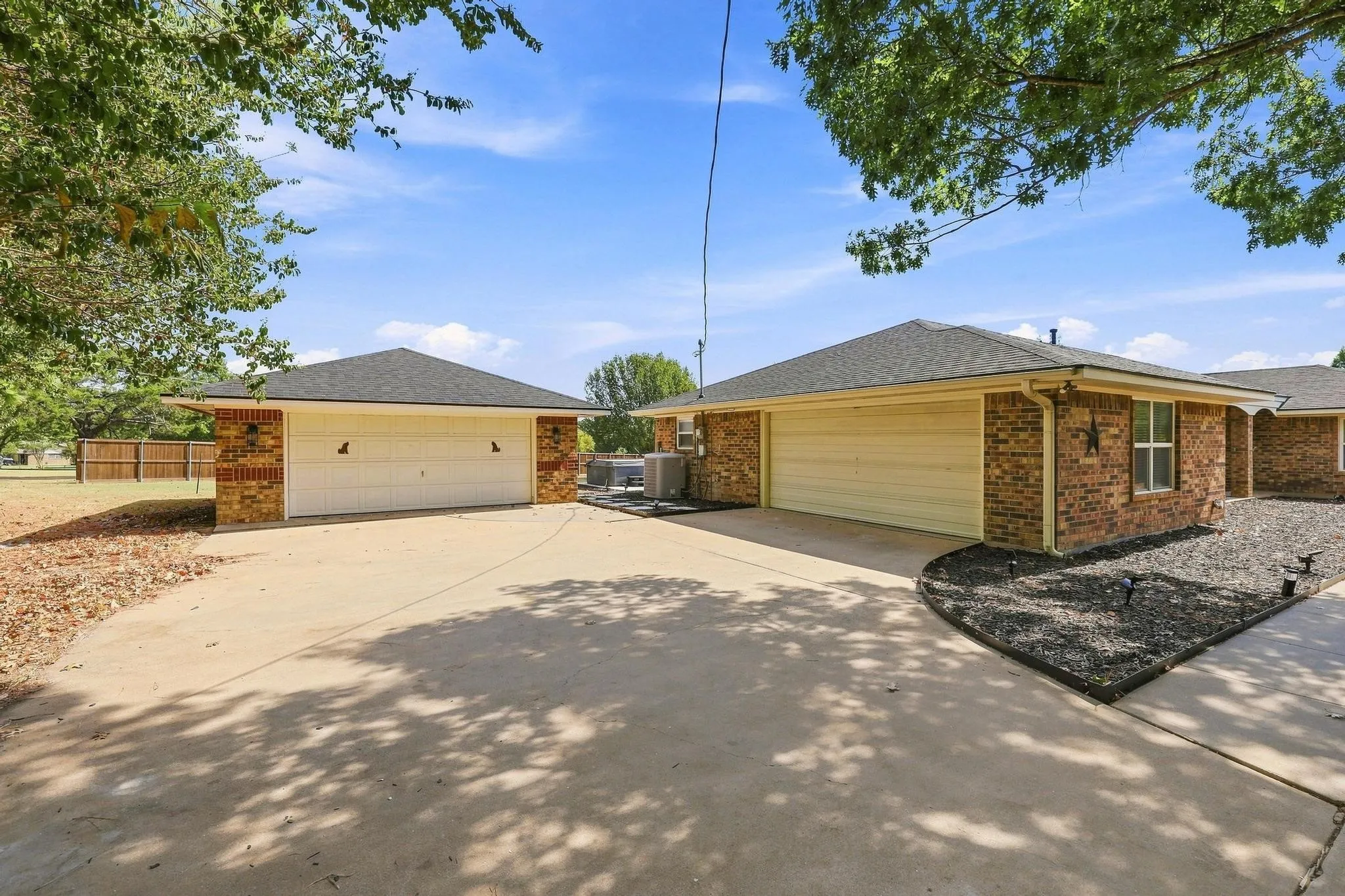 Brick exterior with two attached garages featuring white garage doors, a concrete driveway, and a landscaped bed with dark rock
