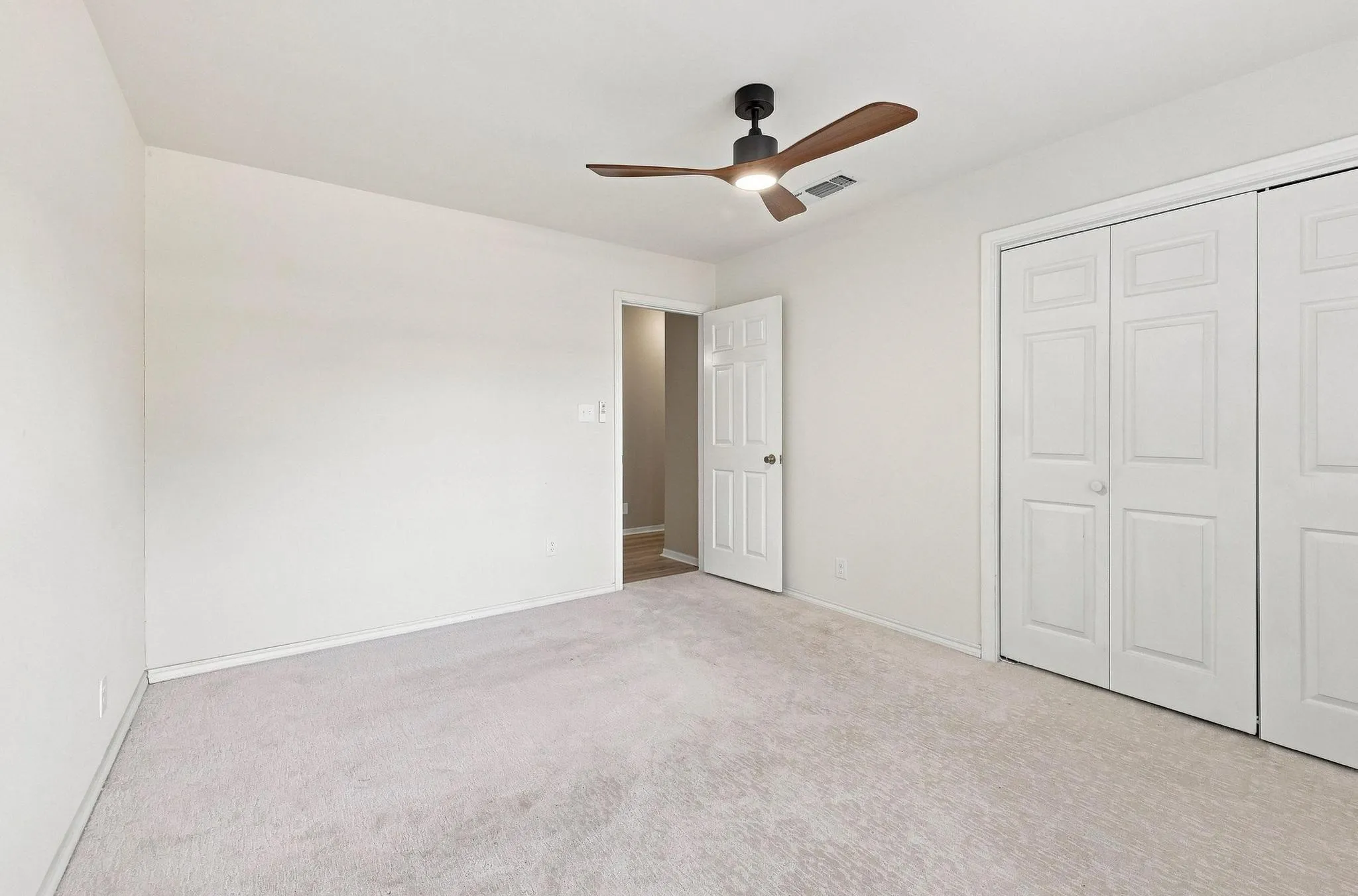 Light-colored carpeting, white walls, and a contemporary ceiling fan with a wood-finish blades