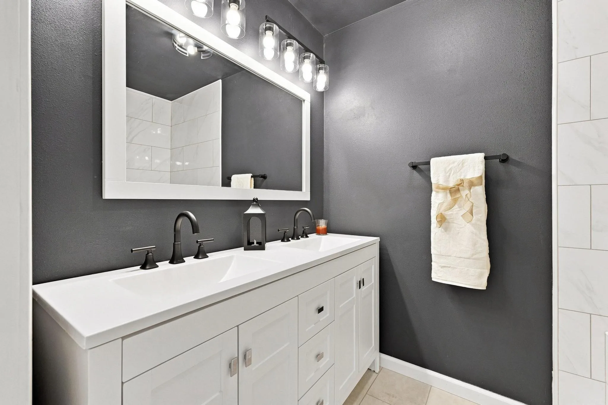 Double vanity with integrated sinks, white countertop, matte black fixtures, and framed mirror with integrated lighting
