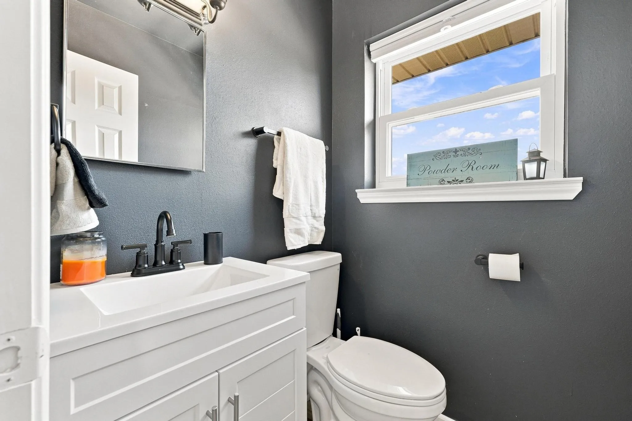 White vanity with integrated sink, matte black faucet, wall-mounted mirror, and a single window