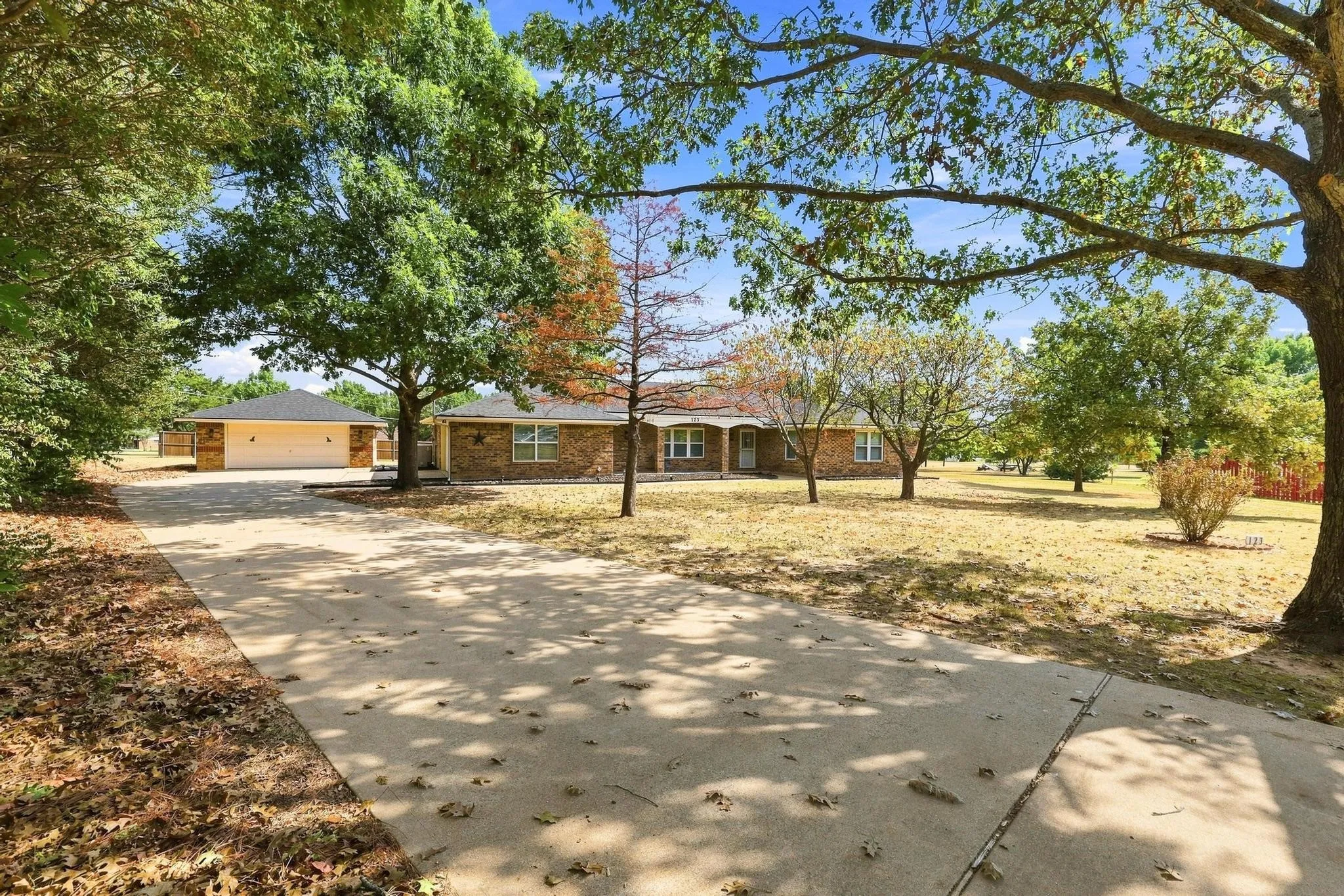 Expansive property featuring a brick-clad residence, detached garage structure, and mature trees