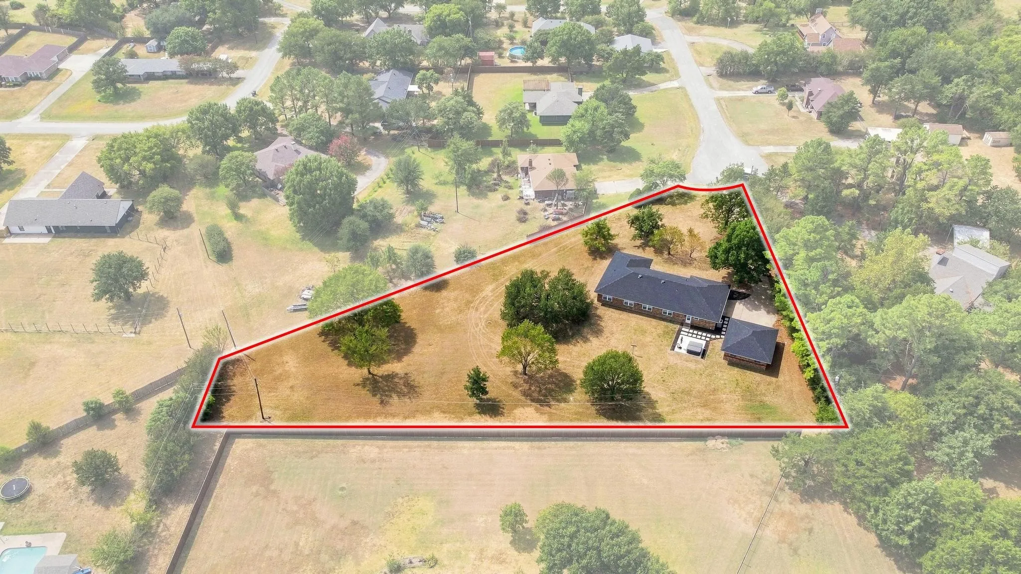 Expansive property featuring a single-story residence, detached outbuilding, mature trees, and a defined lot boundary
