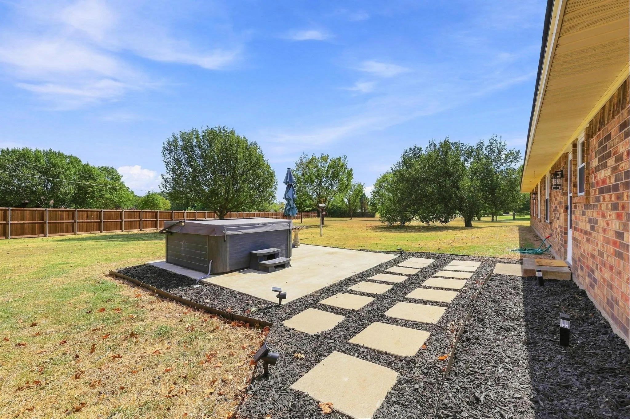 Expansive backyard featuring a hot tub, concrete patio, stepping stone pathway, and brick exterior