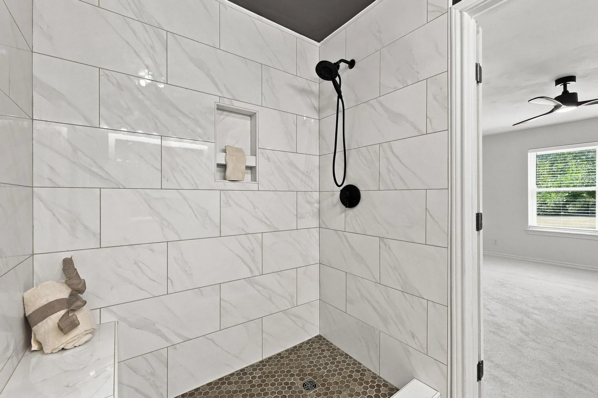 Shower with large format white tile, built-in niche, and dark hexagonal floor tile