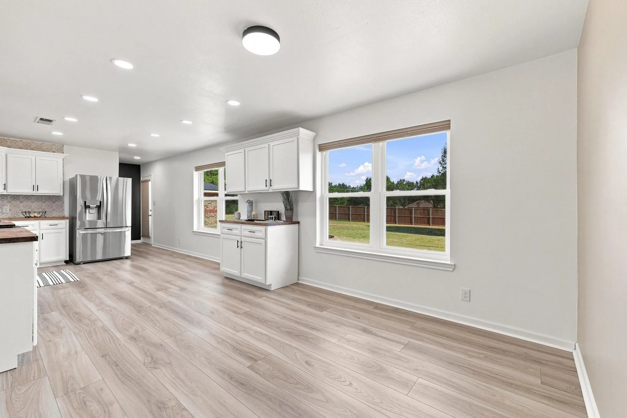 Bright open-concept living area with light wood-finish flooring, white cabinetry, and stainless steel appliances