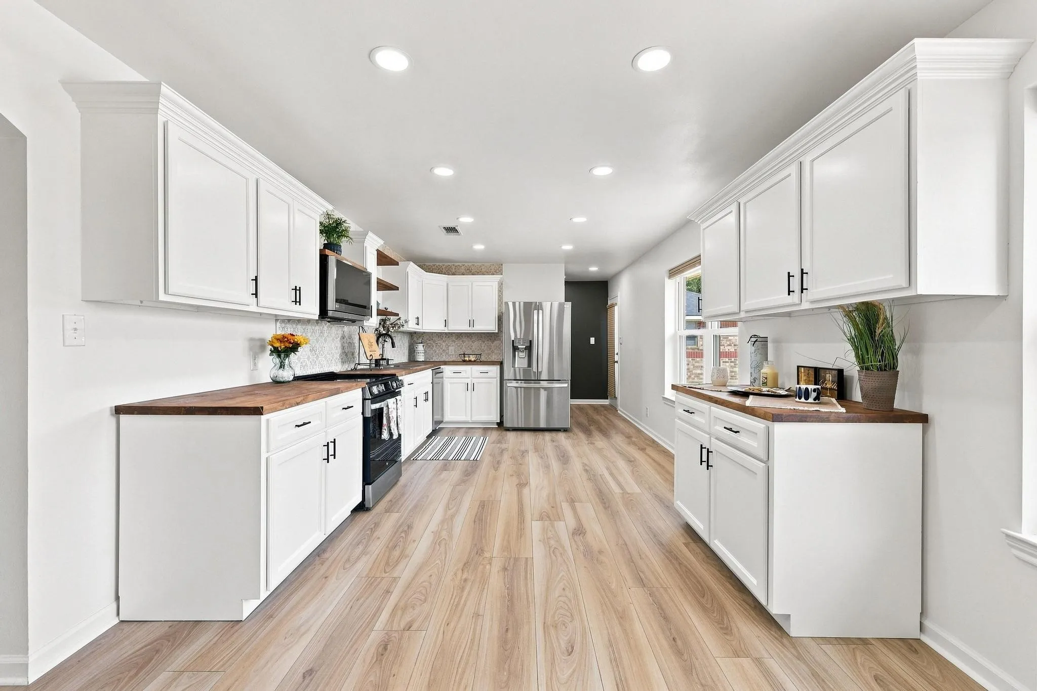 Modern kitchen featuring white cabinetry, light wood-finish flooring, dark wood-tone countertops, stainless steel appliances, and recessed lighting