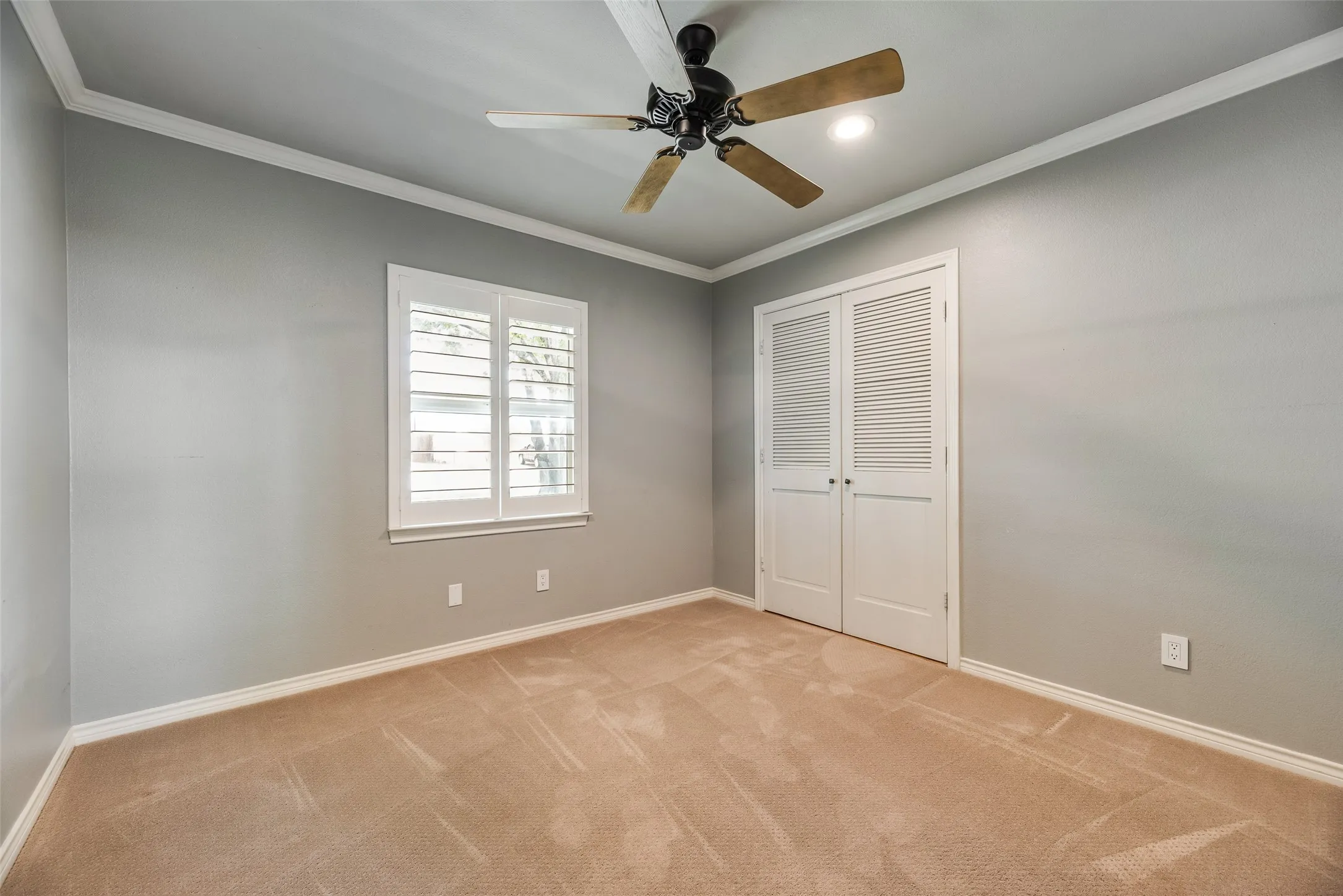 Unfurnished bedroom featuring ornamental molding, light carpet, ceiling fan, and a closet