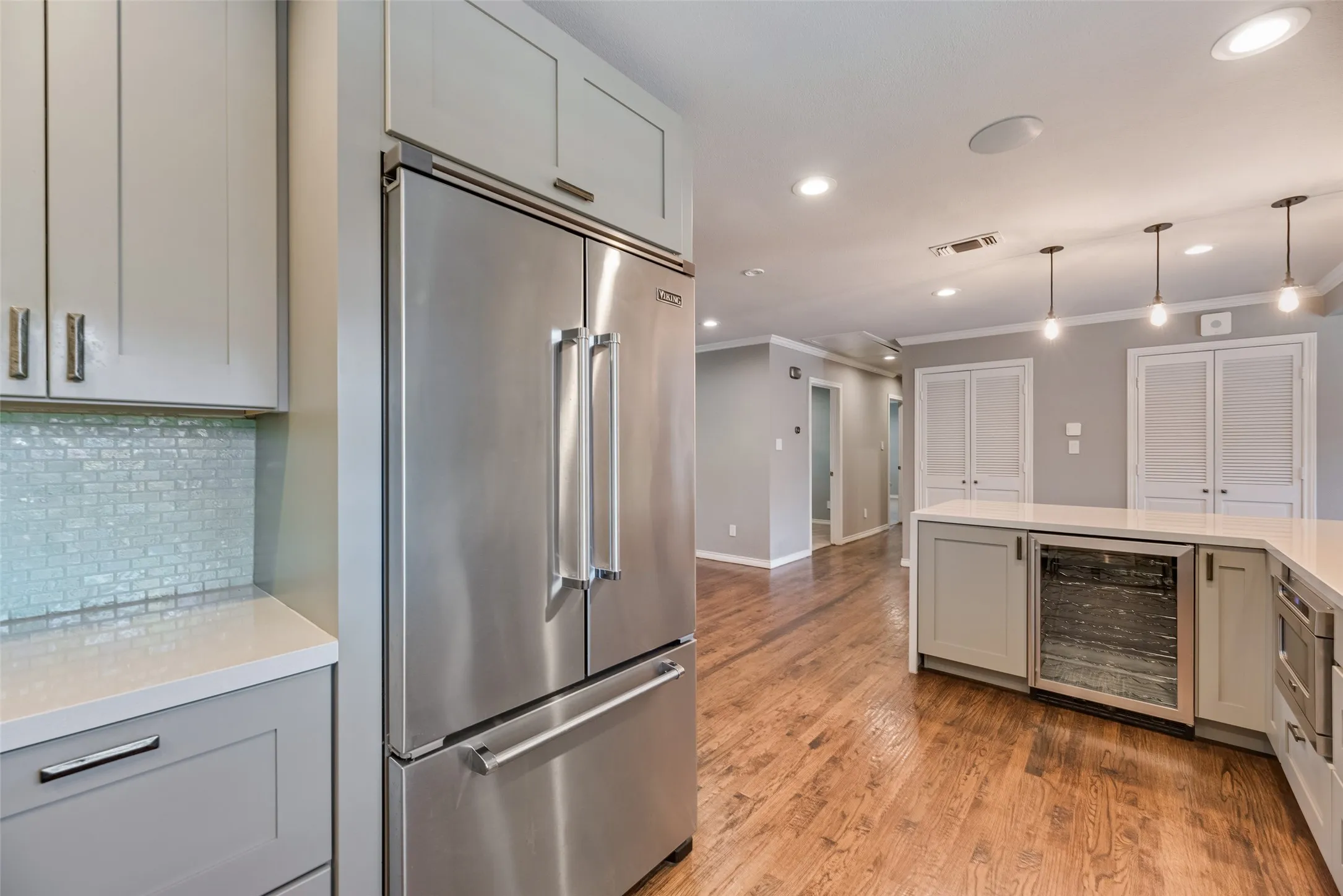 Kitchen featuring high end refrigerator, wine cooler, gray cabinetry, light stone countertops, and ornamental molding