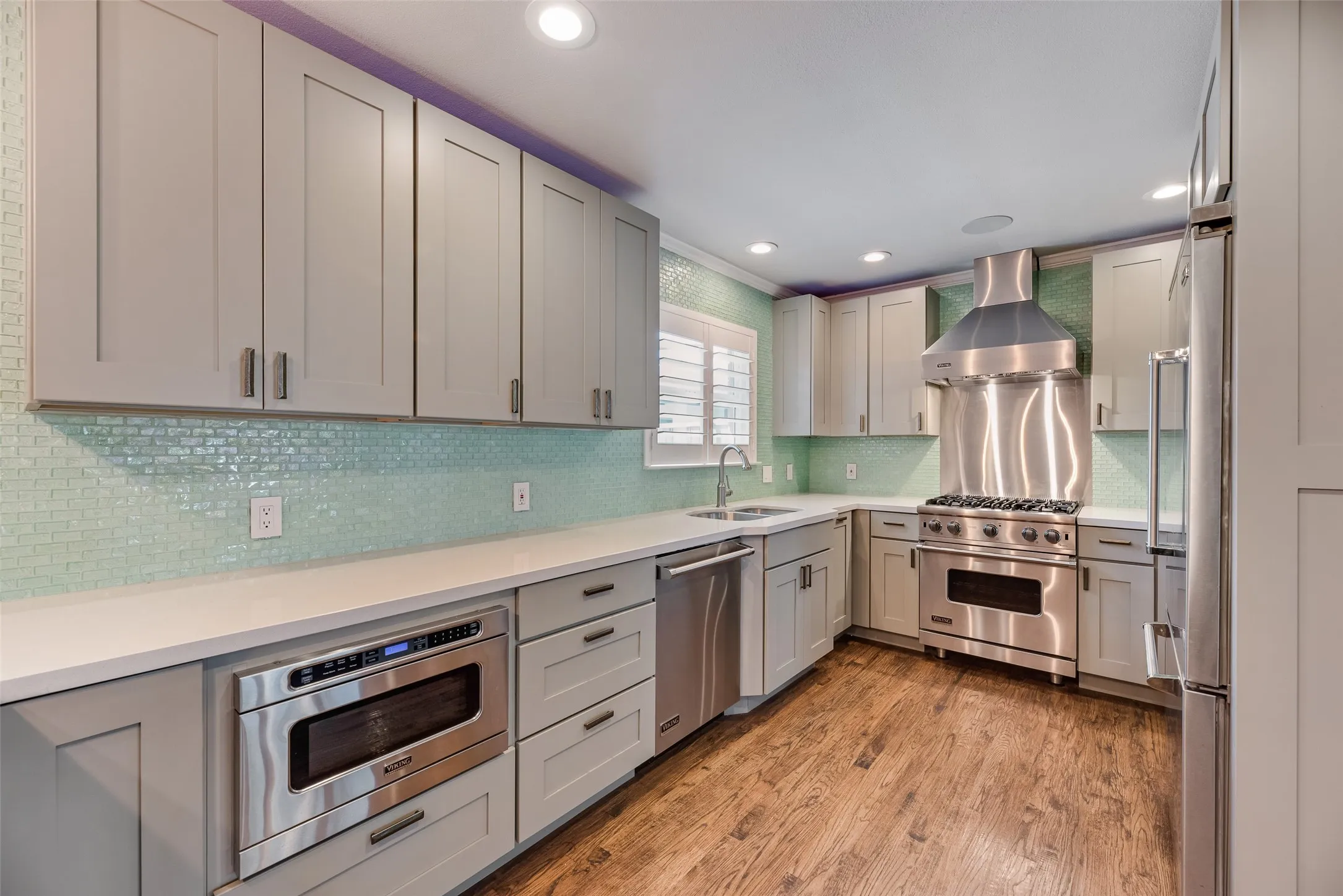 Kitchen featuring high end appliances, light wood-style floors, gray cabinets, tasteful backsplash, and recessed lighting