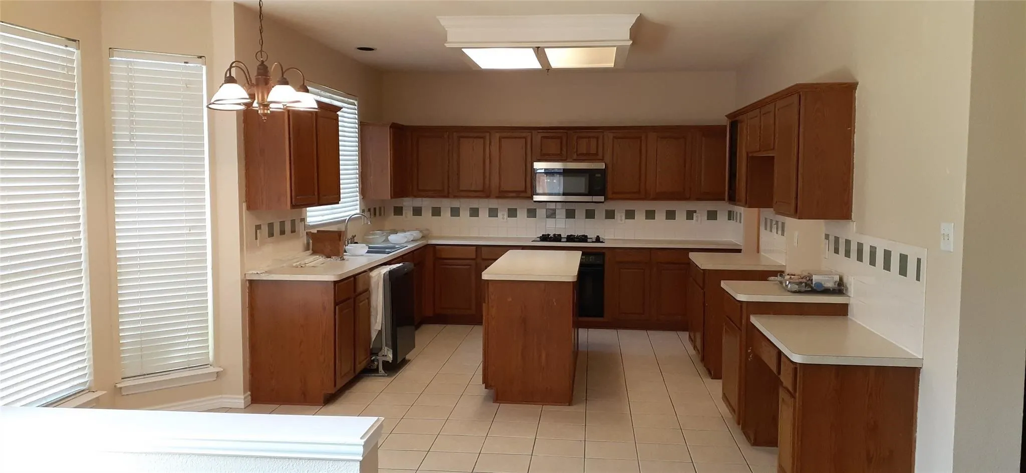Kitchen featuring wood-finish cabinetry, a central island, light-toned countertops, and a tile backsplash